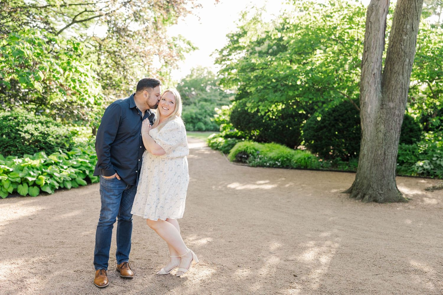 A couple shares an intimate moment on a tree-lined garden path.