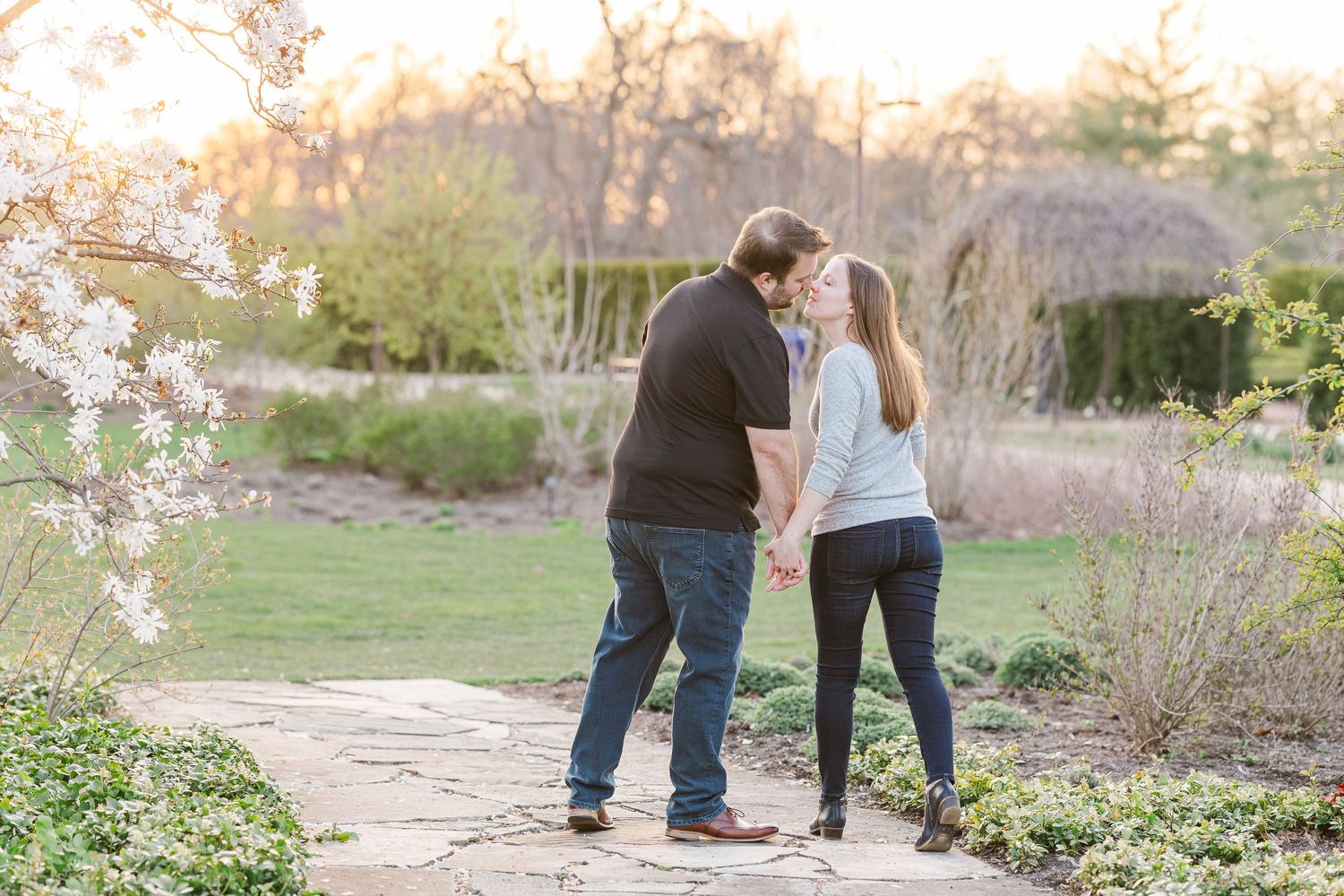 Couple walking hand in hand along garden path surrounded by spring blossoms at sunset.