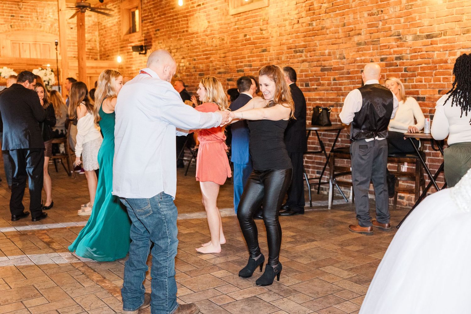 Wedding guests dancing together at a reception in a rustic industrial venue with exposed brick walls.