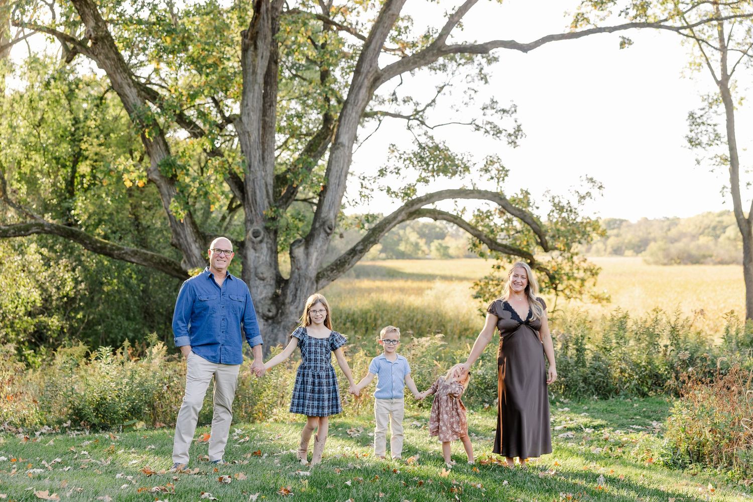 Family of five holding hands in their sunlit backyard during fall family photos in St. Charles, IL.