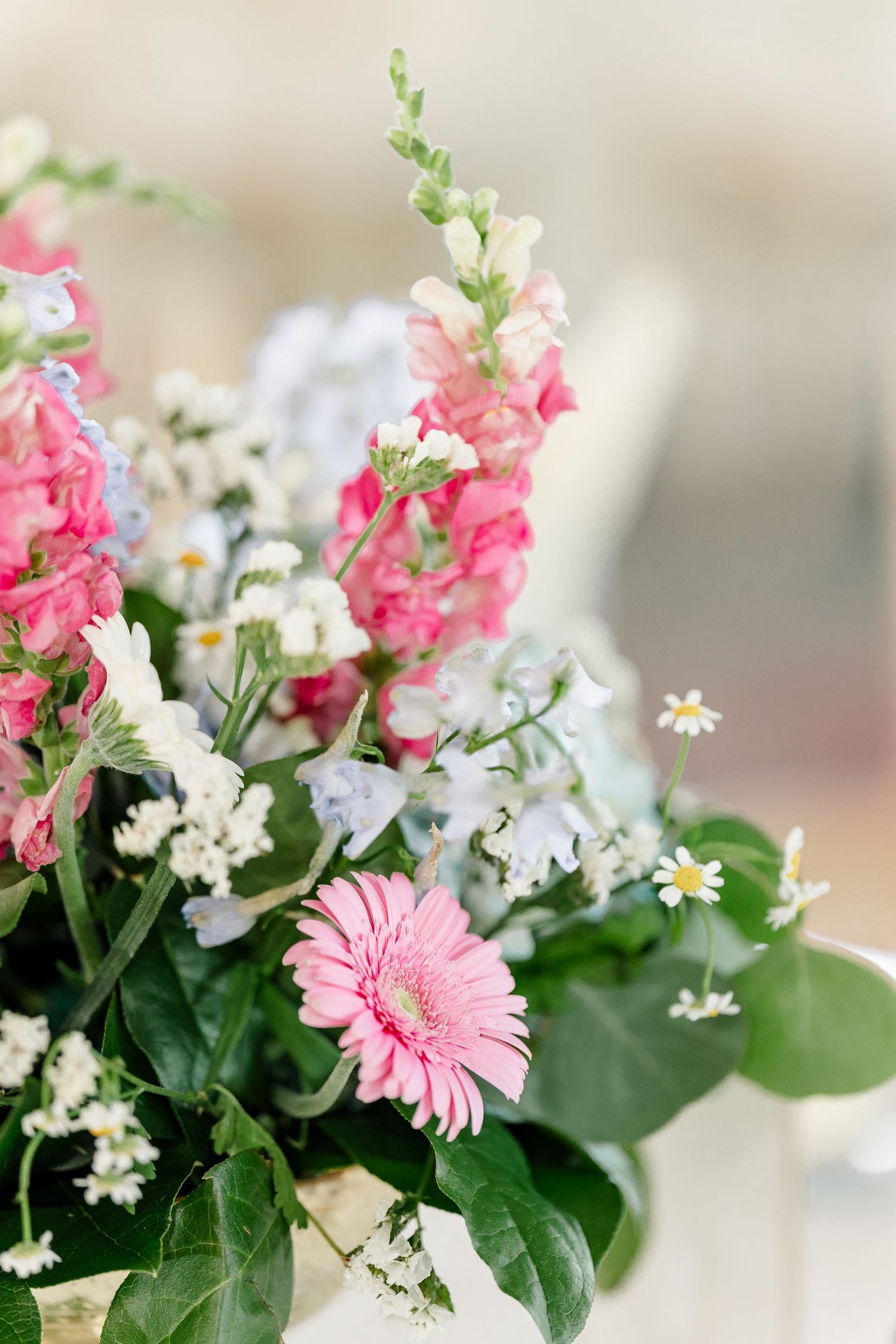 Close-up of elegant wedding floral arrangement featuring pink gerbera daisies, snapdragons, and blue hydrangeas.