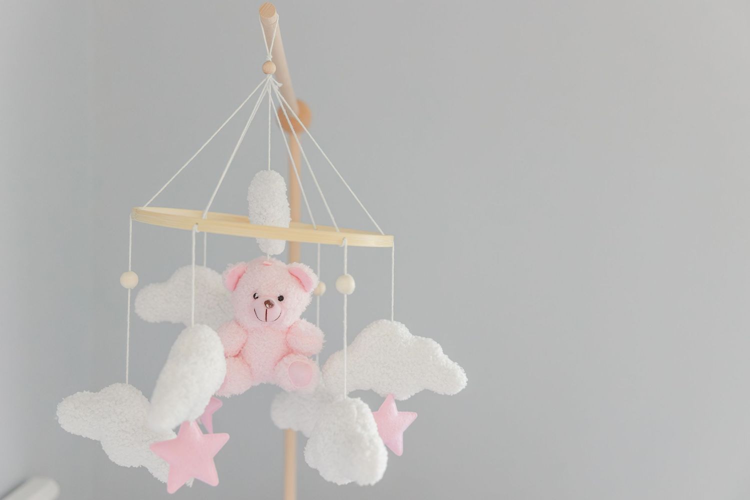 A cute pink teddy bear baby mobile with white clouds and pink stars hangs against a gray background.