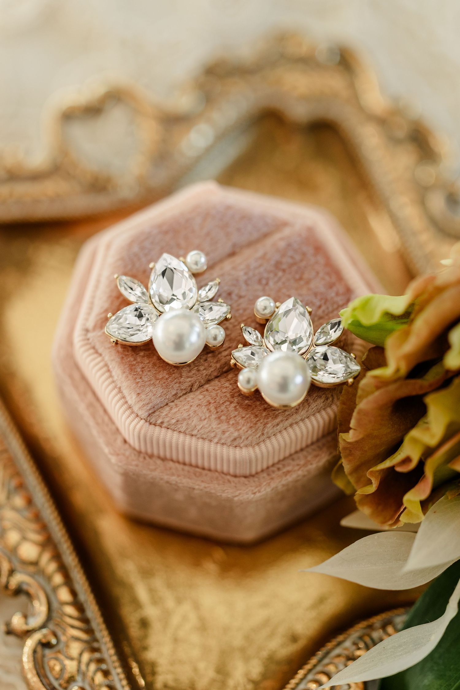 Pearl and crystal cluster bridal earrings resting on a blush velvet octagonal ring box atop an ornate gold tray with autumn flowers.
