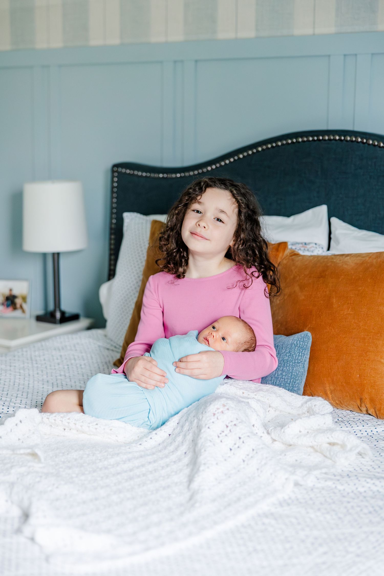 Big sister holding newborn on bed during lifestyle newborn session in Crystal Lake, Illinois