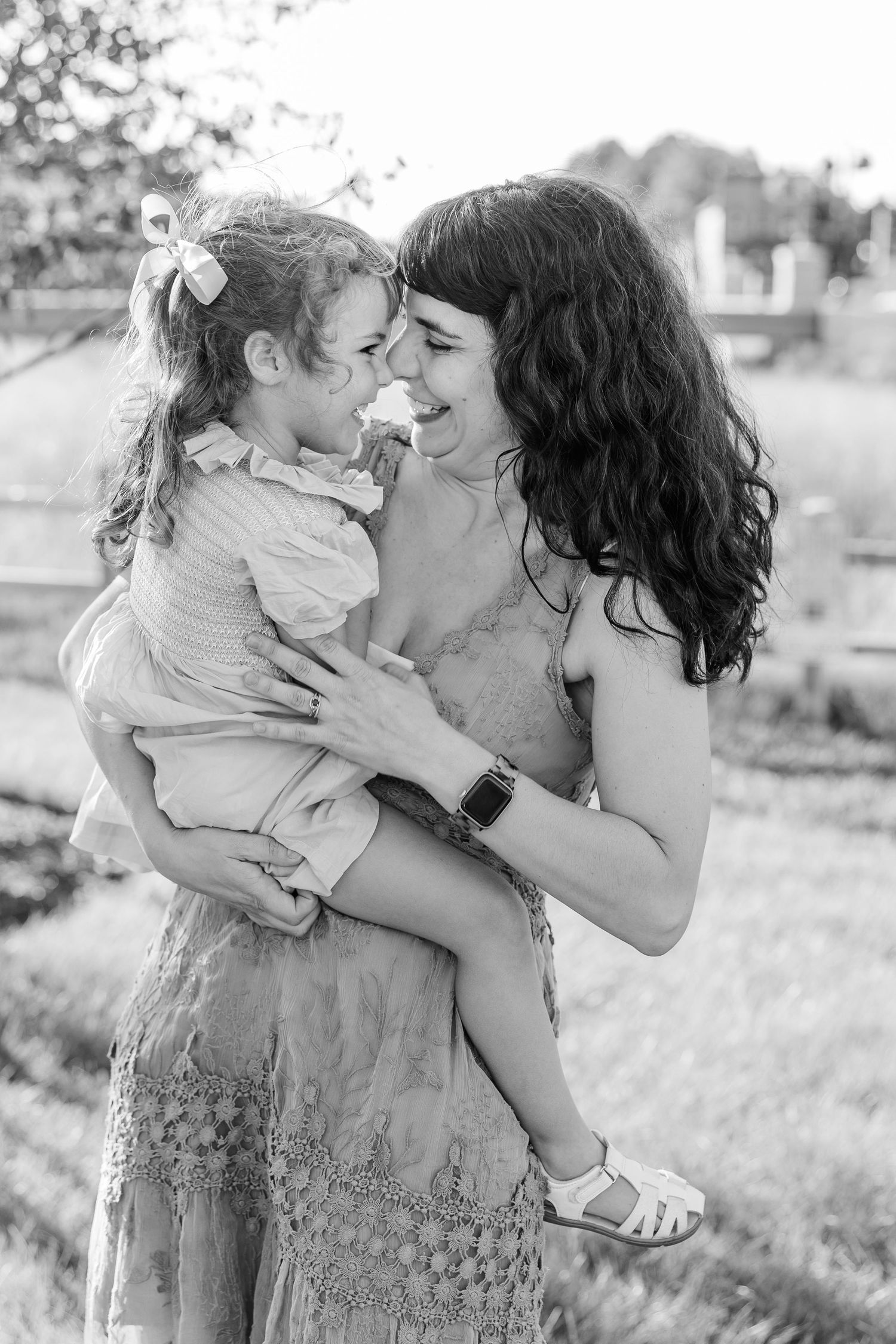 Mother laughing while holding her young daughter close in a black and white outdoor portrait.