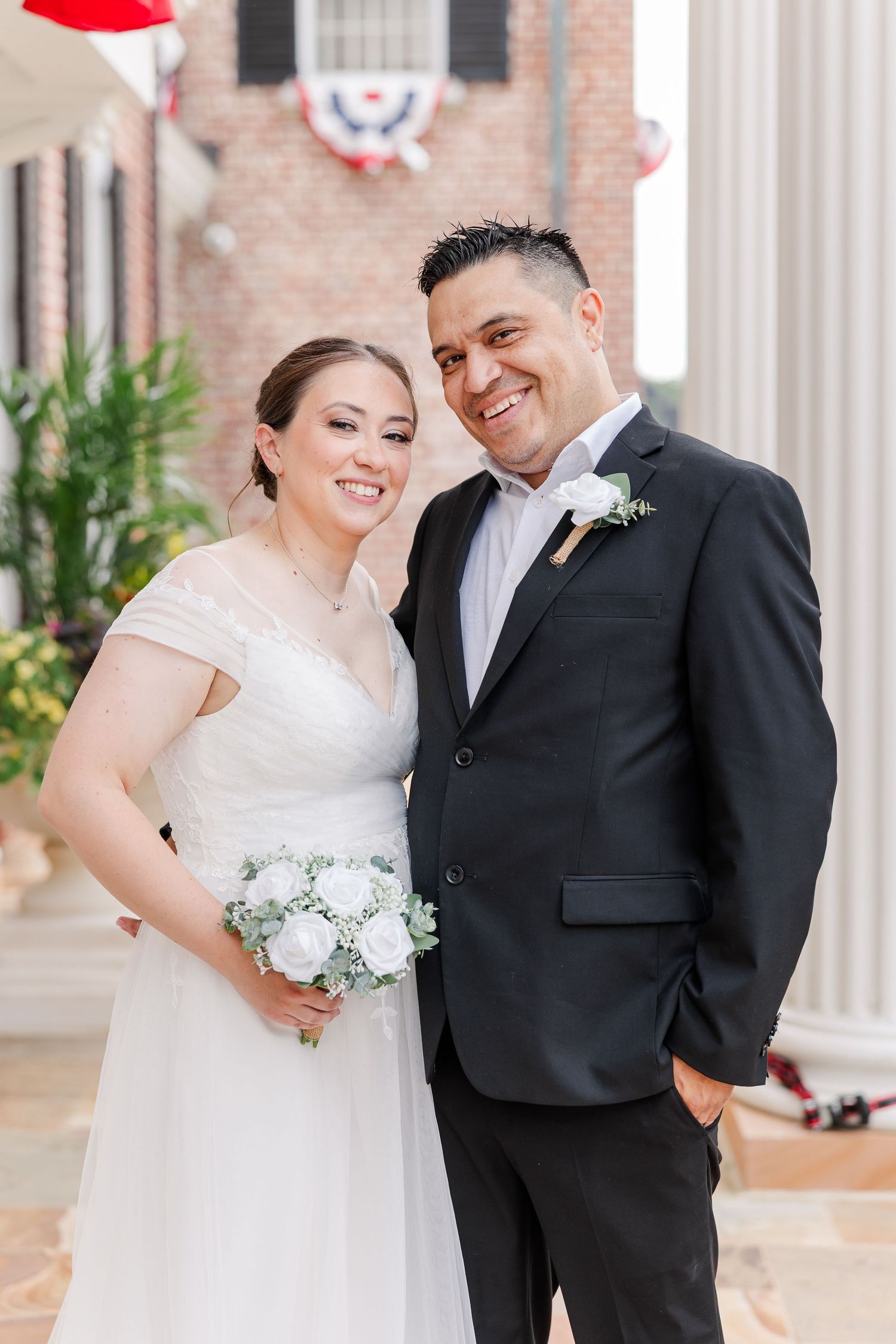 Smiling bride and groom posing together beneath the white columns at Cantigny Park’s McCormick House.