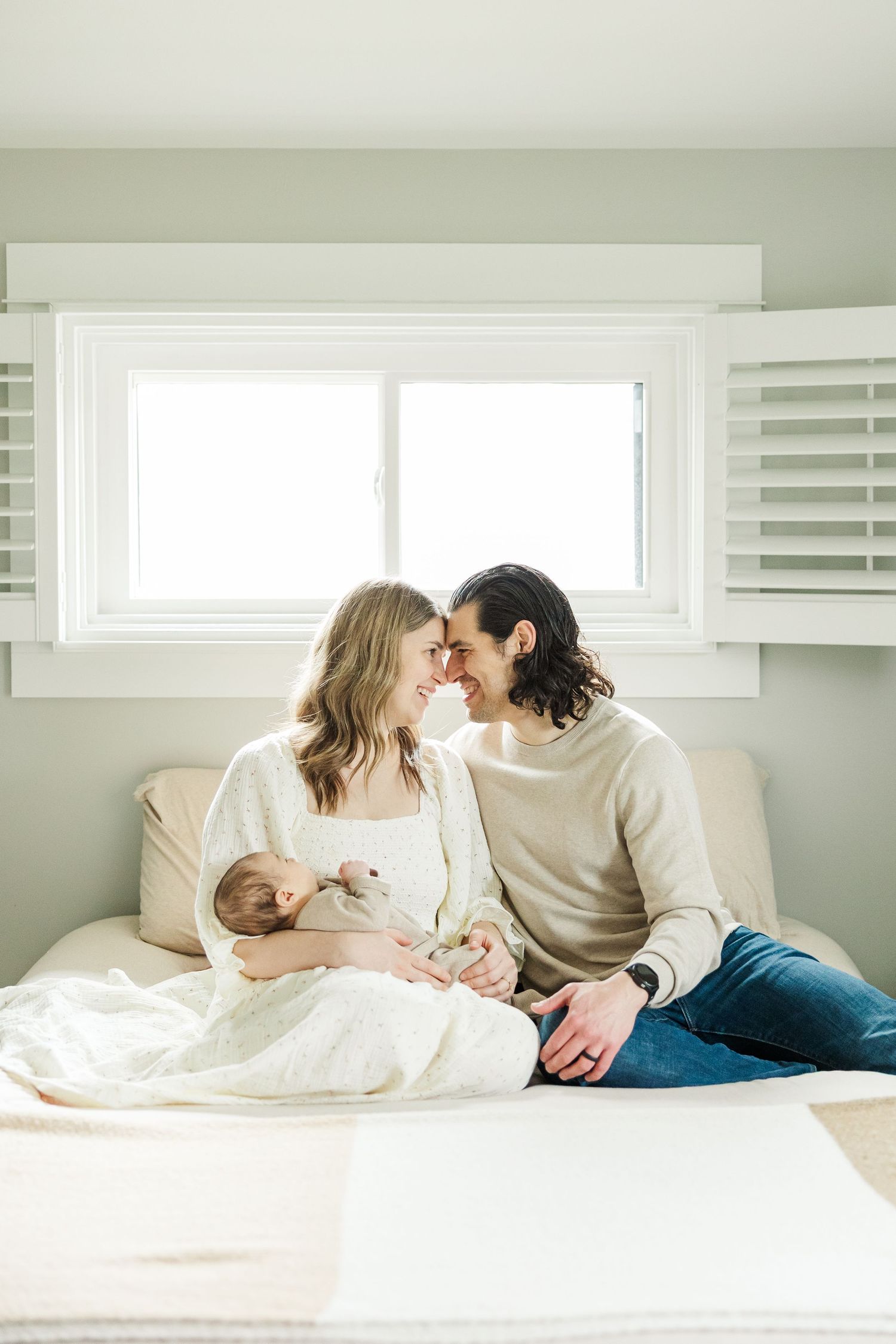 Parents sitting together on their bed holding their newborn baby during an in-home lifestyle newborn photography session in Palatine IL