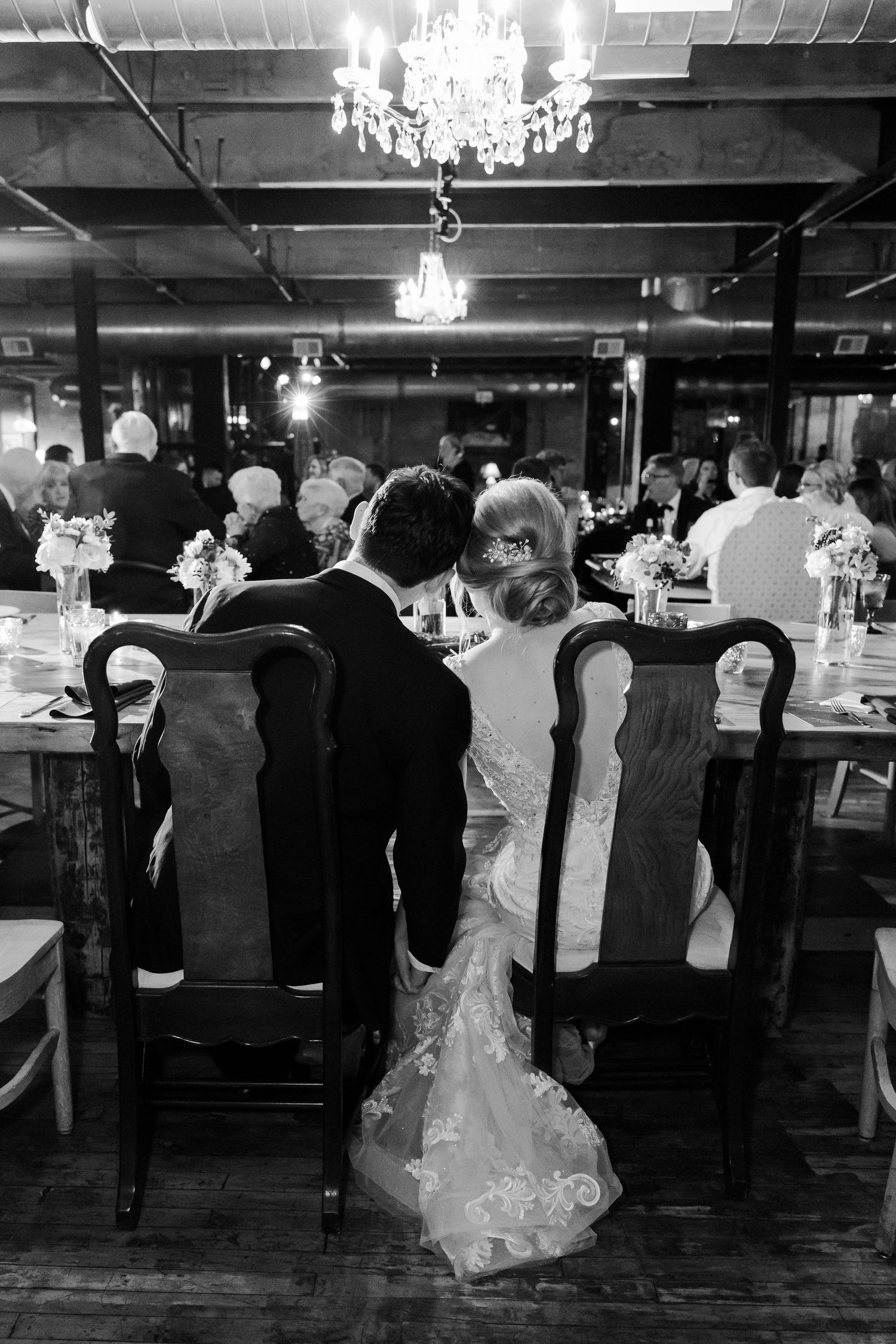 Elegant wedding reception venue with crystal chandeliers and formal table settings in black and white.