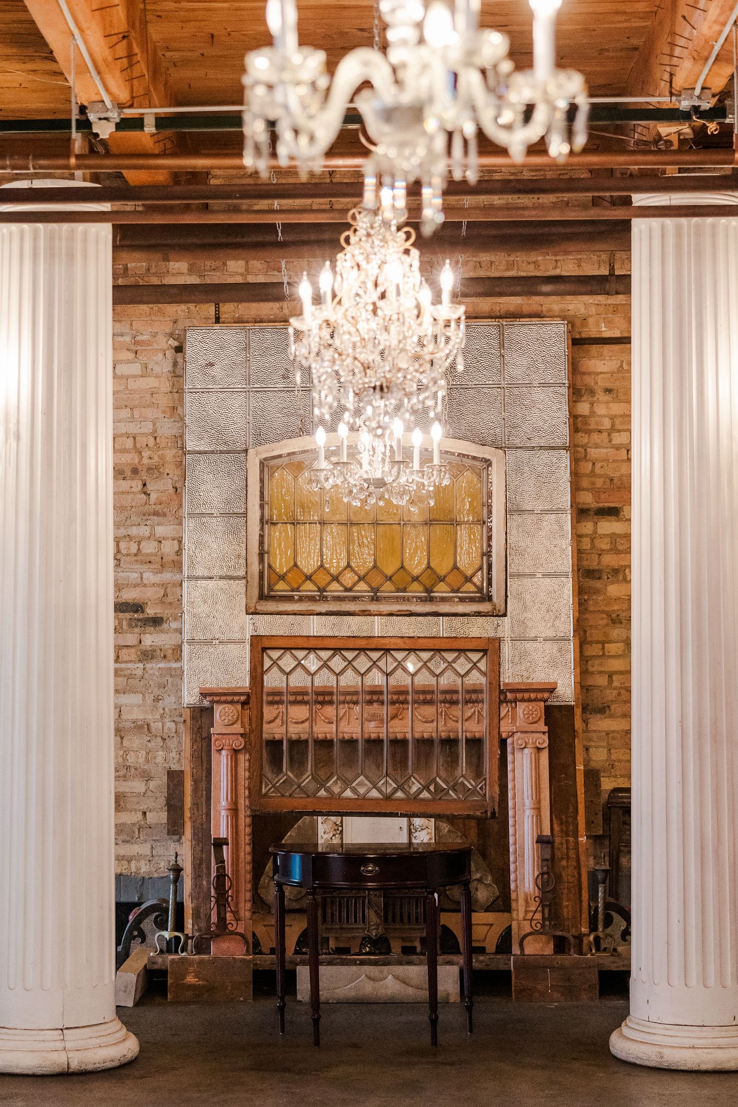 An elegant venue interior with white columns, crystal chandeliers, and exposed brick walls.