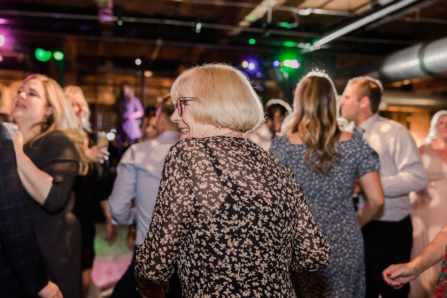 Guests dancing at a wedding reception with colorful party lights in an industrial space.