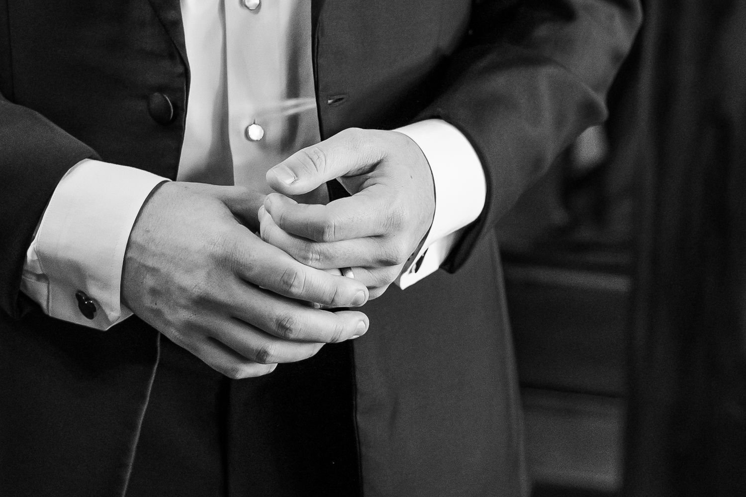 Black and white photo of hands adjusting formal wear cufflinks.