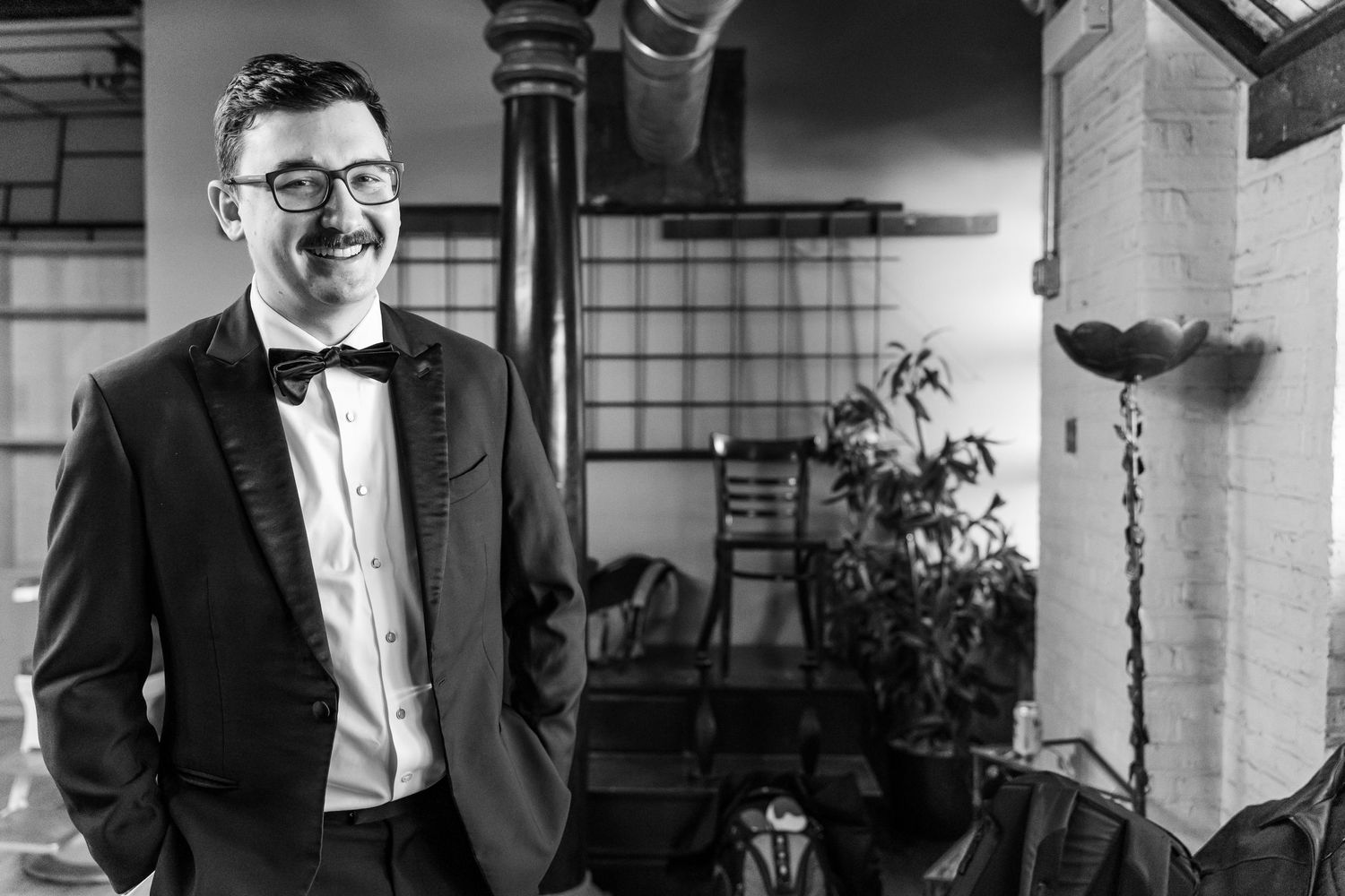 Elegant black and white photo of a person in formalwear standing against a vintage interior.