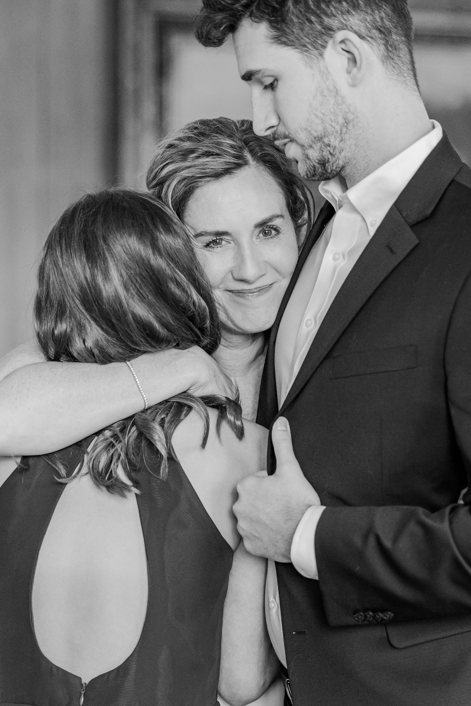 Black and white intimate moment captured between three people in formal attire.