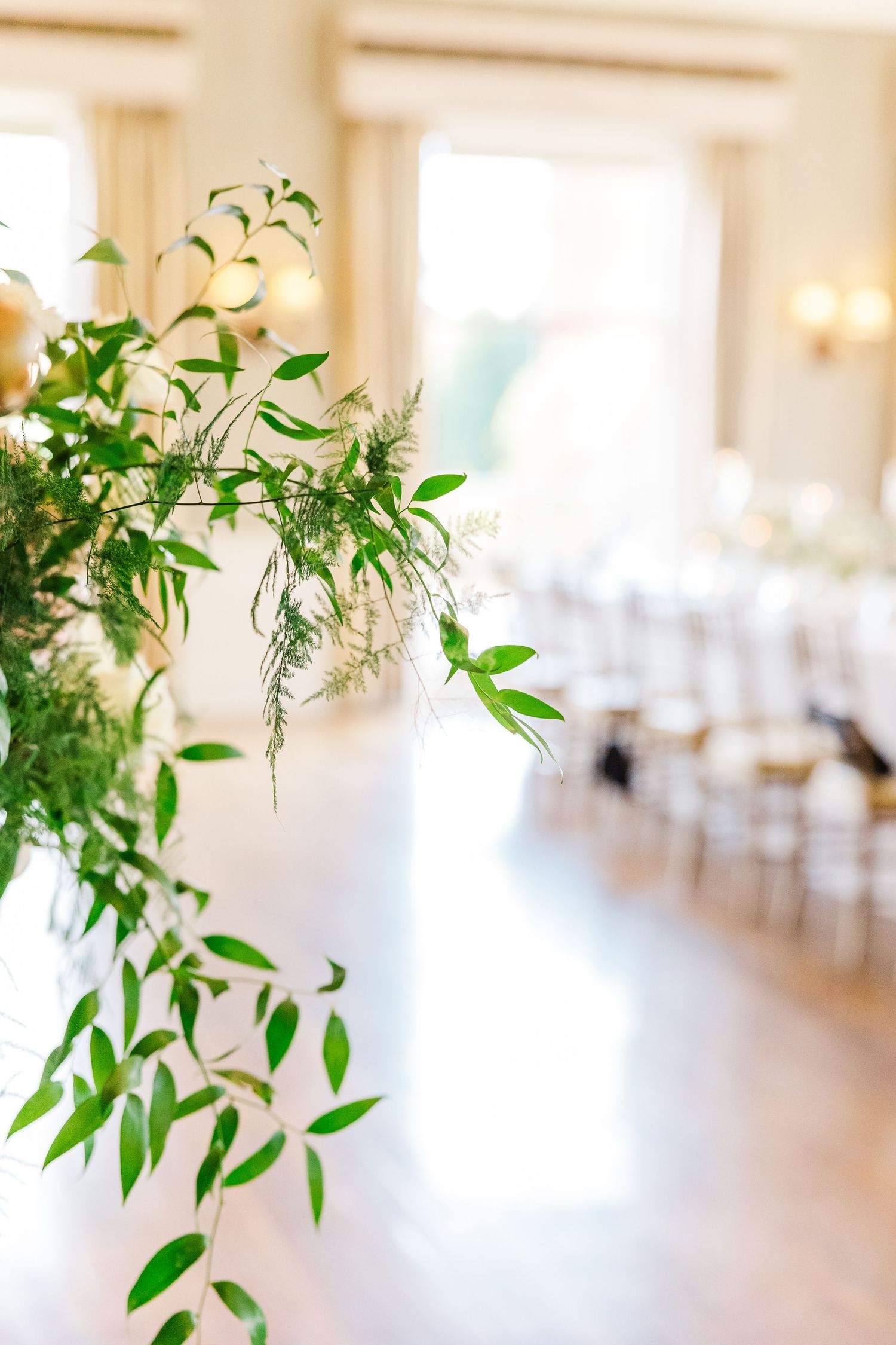 Dreamy interior of an elegant reception hall with hanging greenery and white decor.