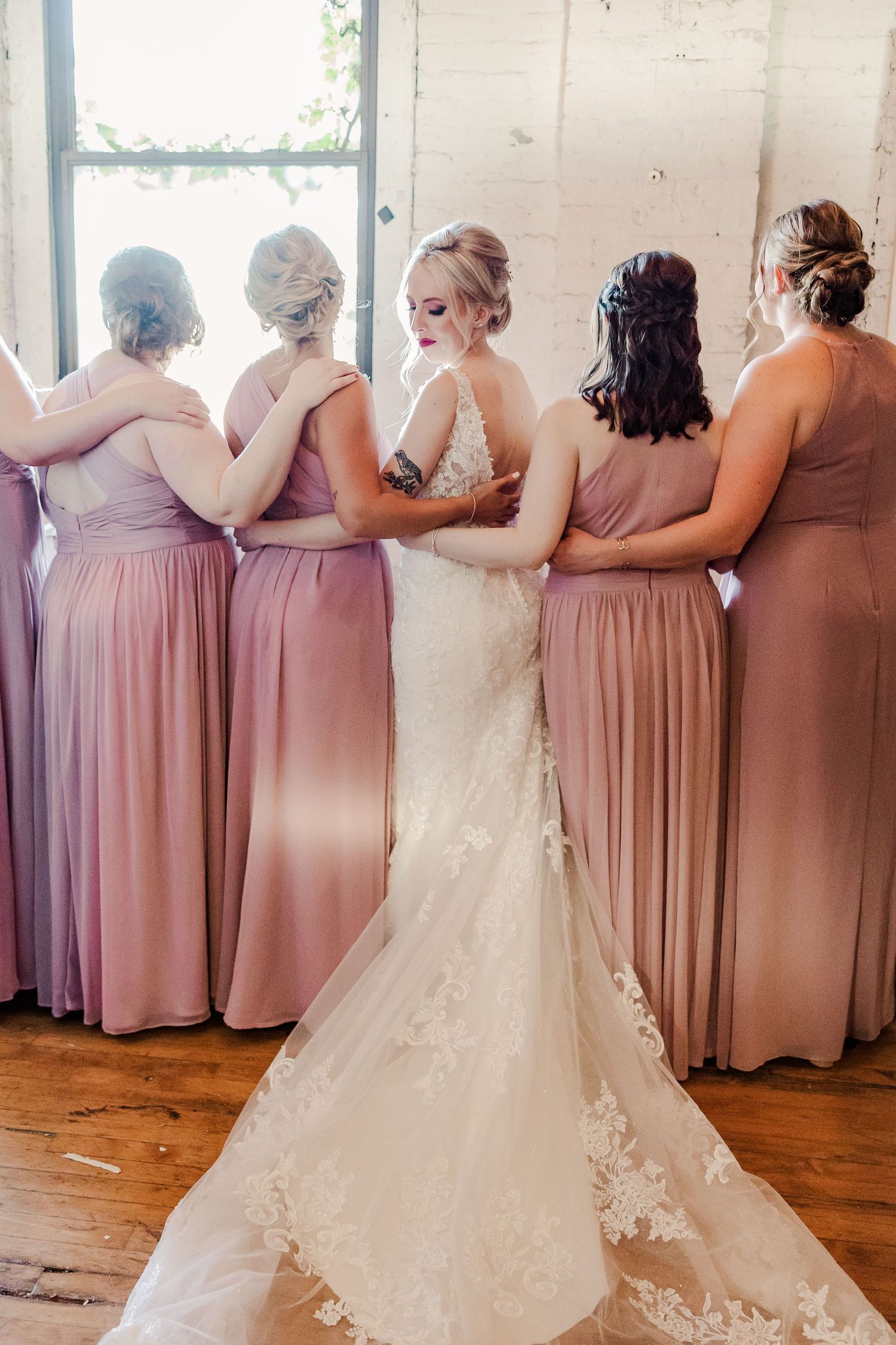 Wedding party stands together in elegant pose showcasing flowing blush gowns and lace wedding dress.