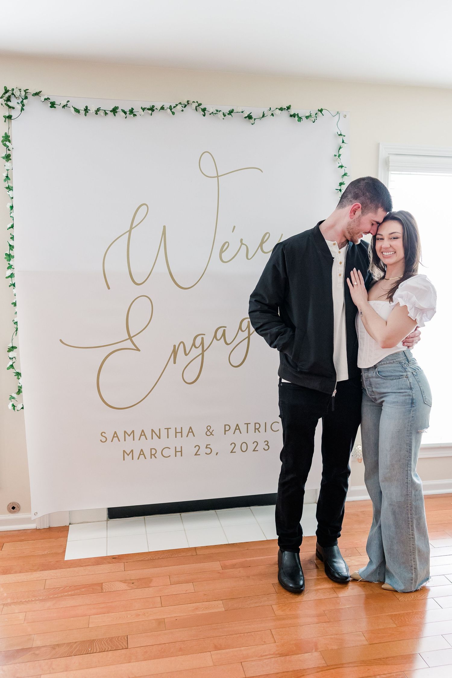 Happy couple sharing intimate moment in front of their engagement announcement backdrop.