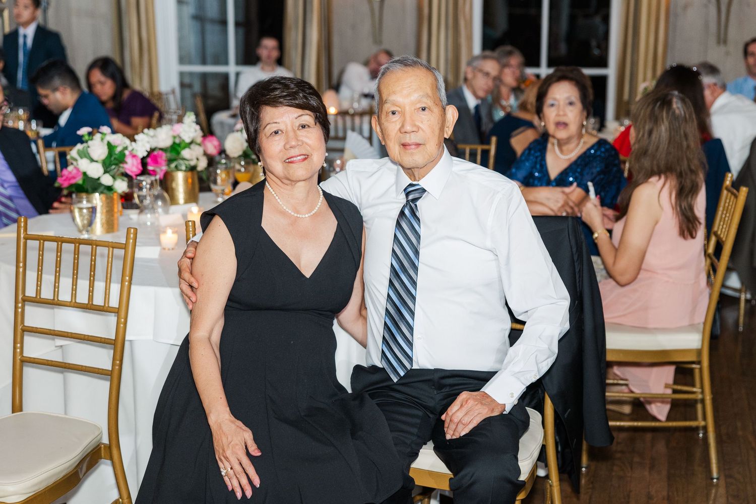 Guests enjoying themselves at an elegant wedding reception with floral centerpieces and gold chairs.