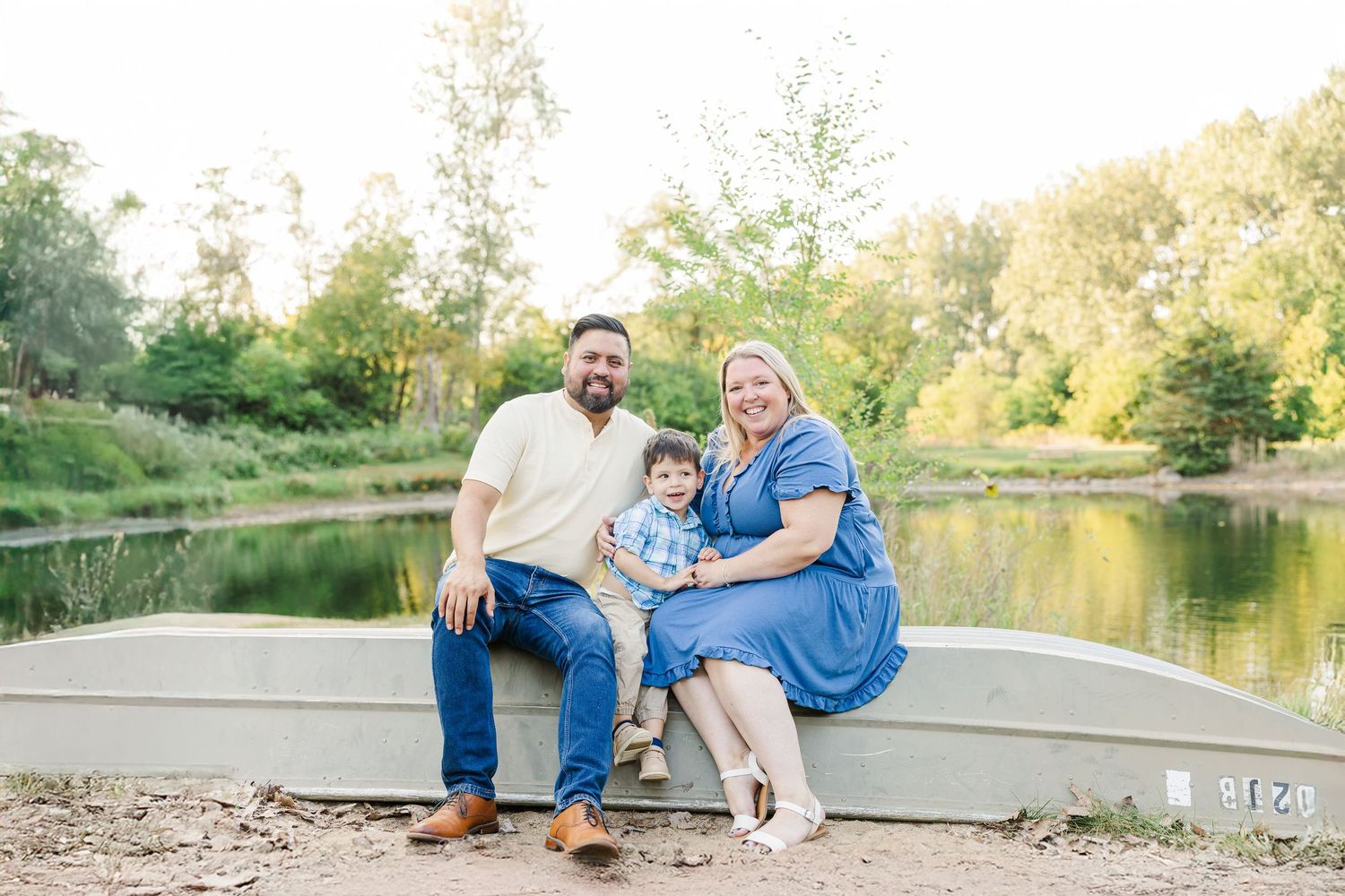 A small group sits together on an aluminum boat by a peaceful pond surrounded by trees on a sunny day.Sorg family portraits at Shamrock Hill