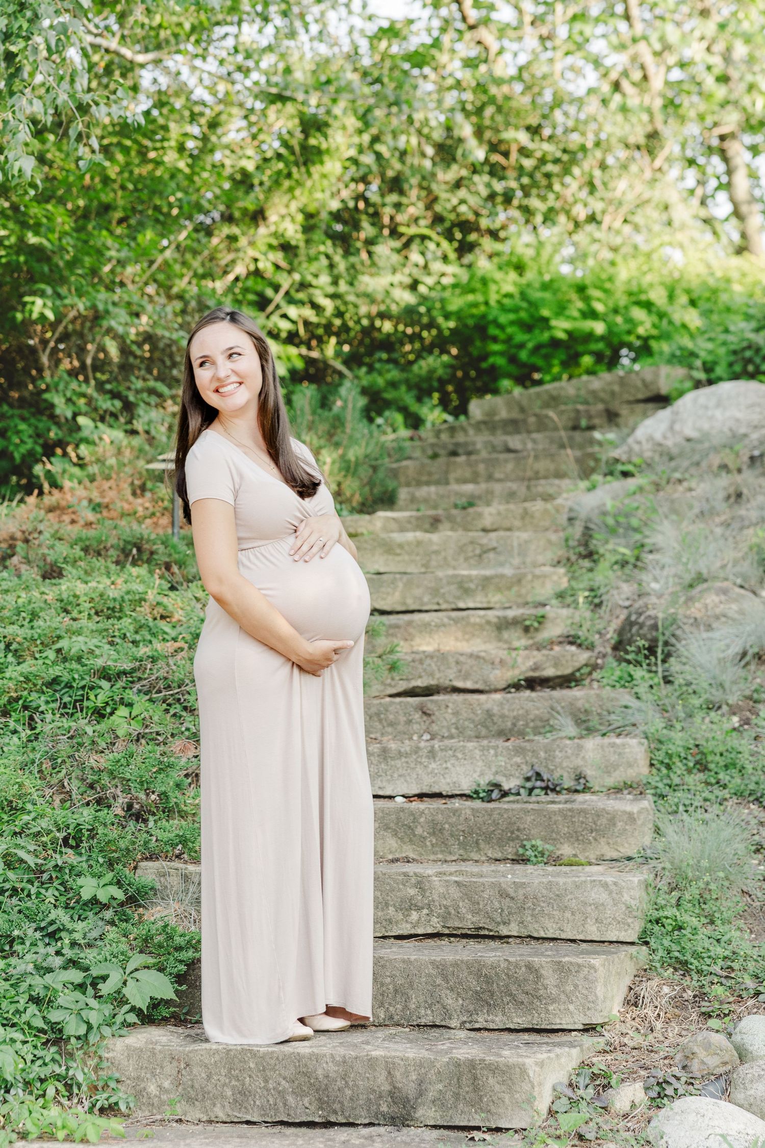 A maternity photo session in a natural outdoor setting with stone steps and lush greenery.