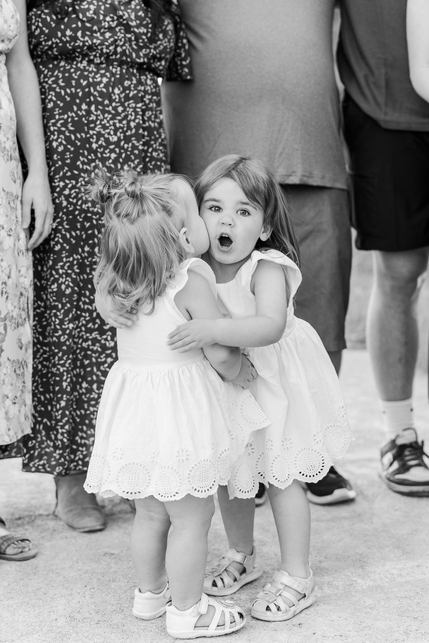 Two young children in white dresses sharing an excited moment together at a gathering.