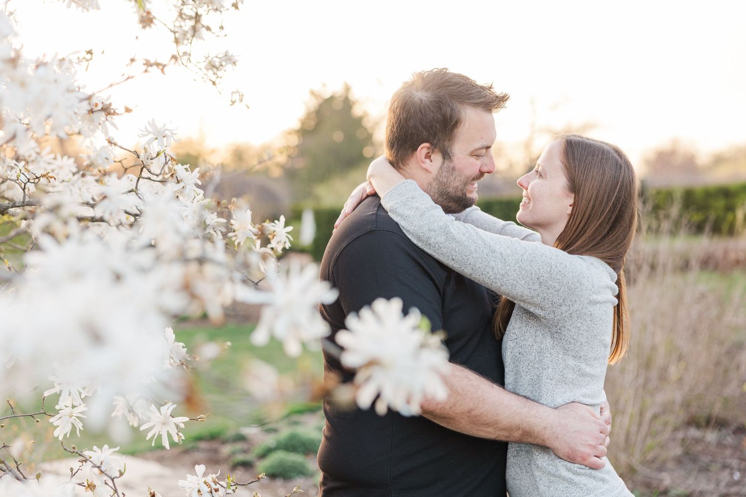 Intimate couple sharing an embrace among white spring blossoms in soft natural light.