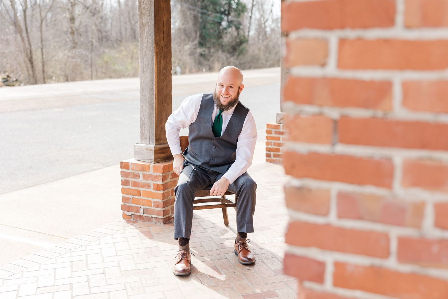 Person in formal attire sitting on wooden chair against brick wall.