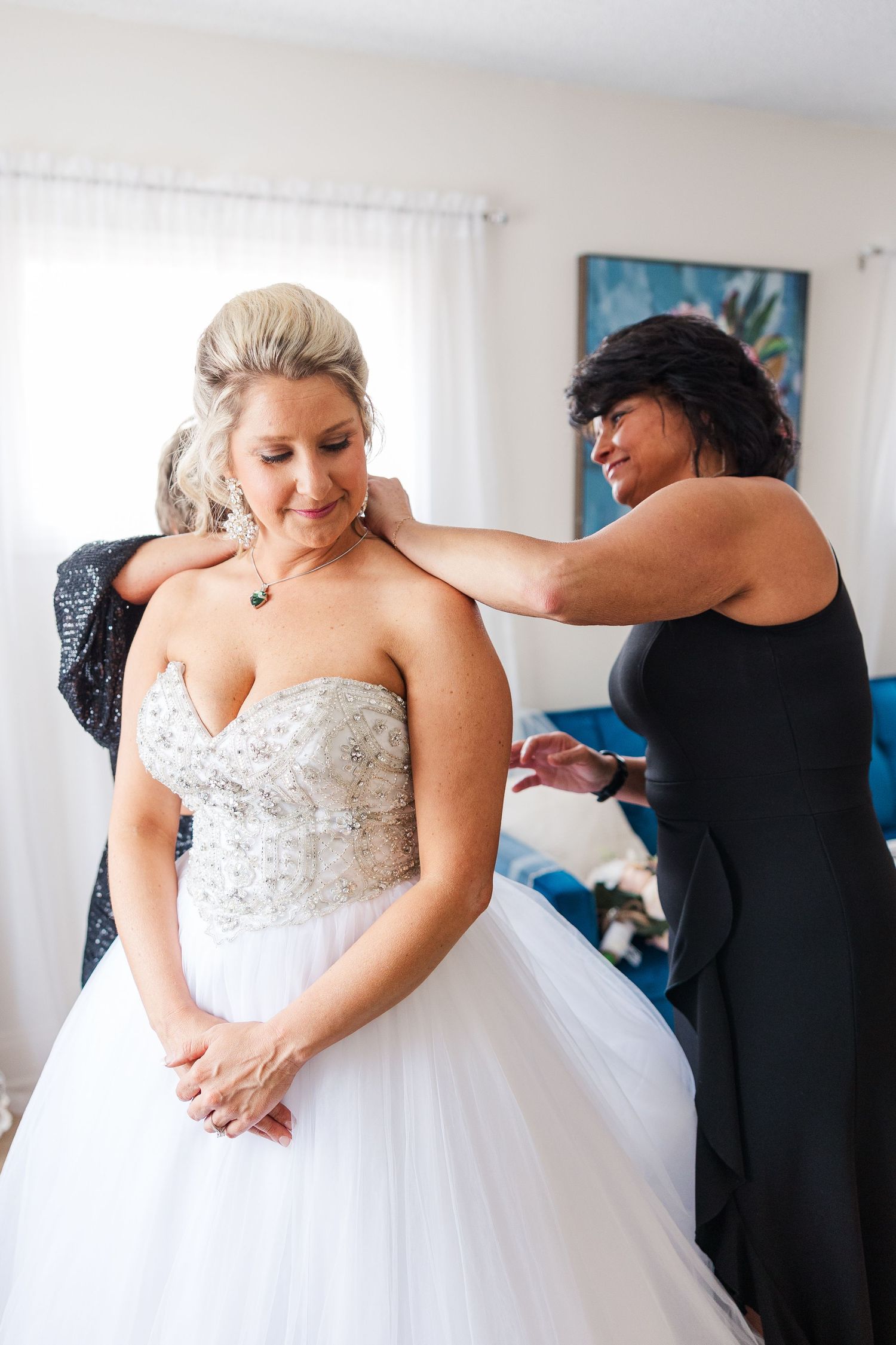 Final adjustments being made to an intricately beaded wedding dress in a bright room.