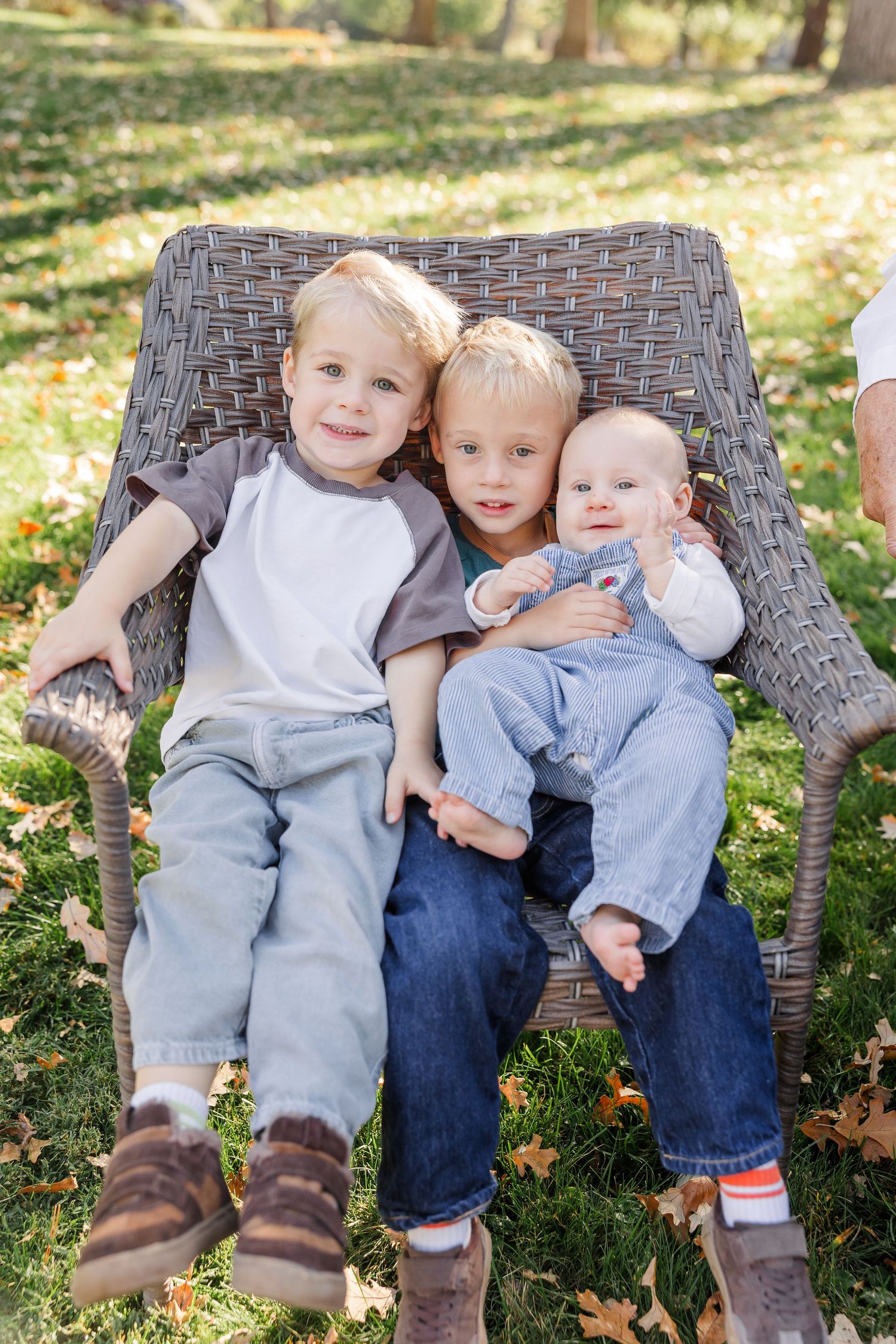 Three young siblings cuddle together in a wicker chair outdoors during fall.