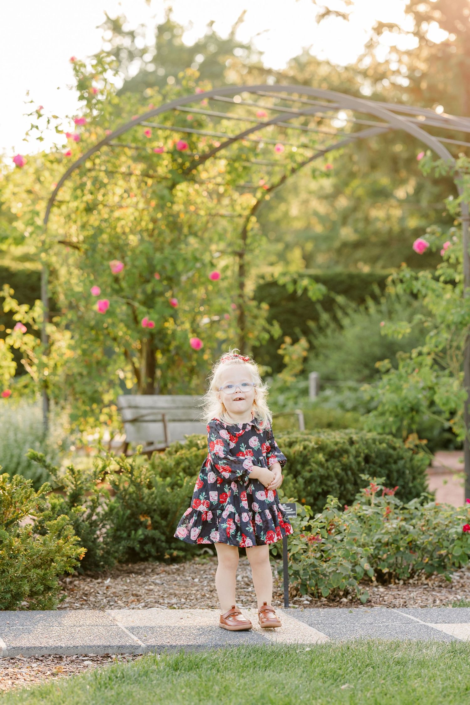 Caroline smiling in her floral dress beneath a rose-covered garden arch at Cantigny Park.