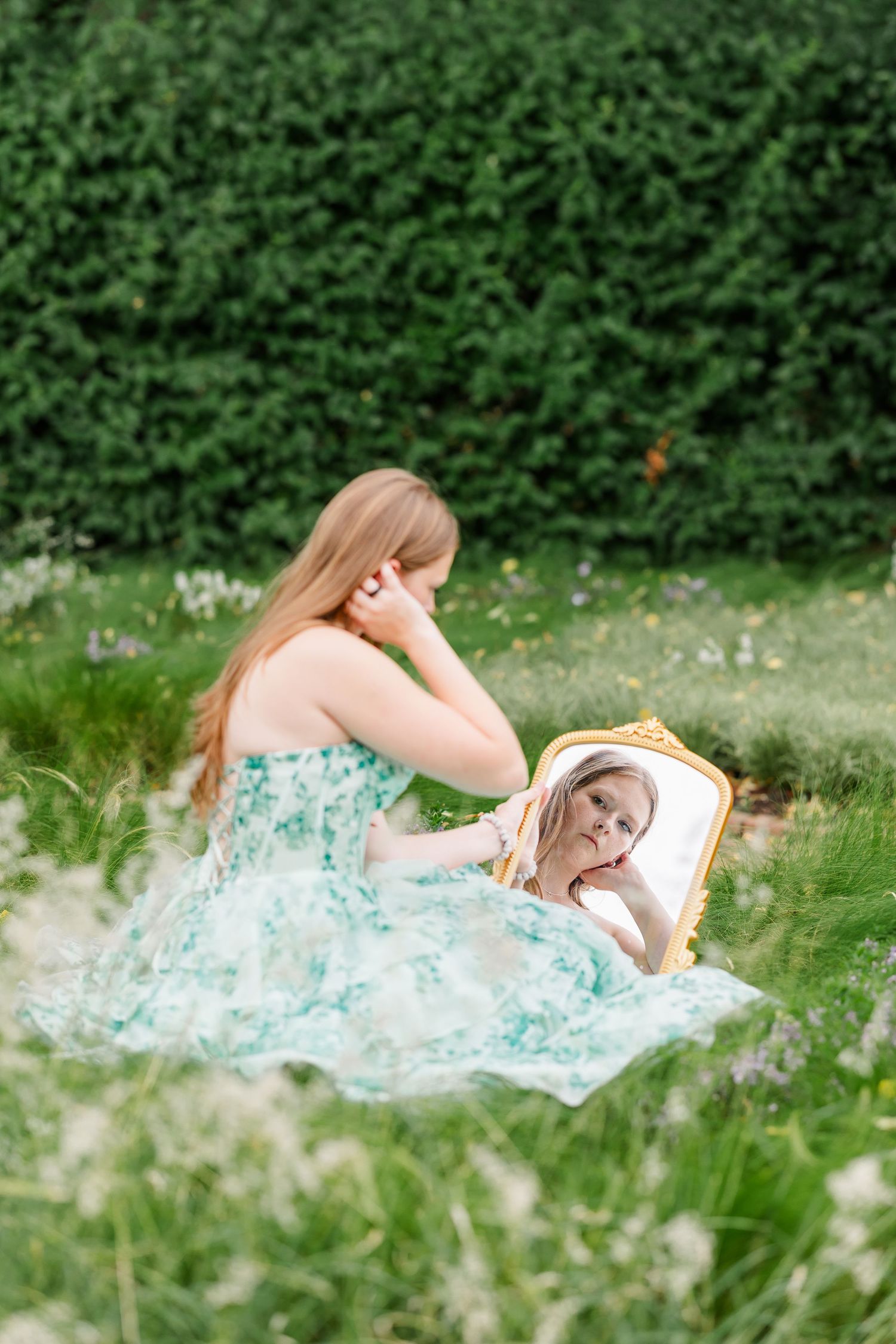 Samantha looks into a vintage gold mirror while sitting among wildflowers during her creative senior session.