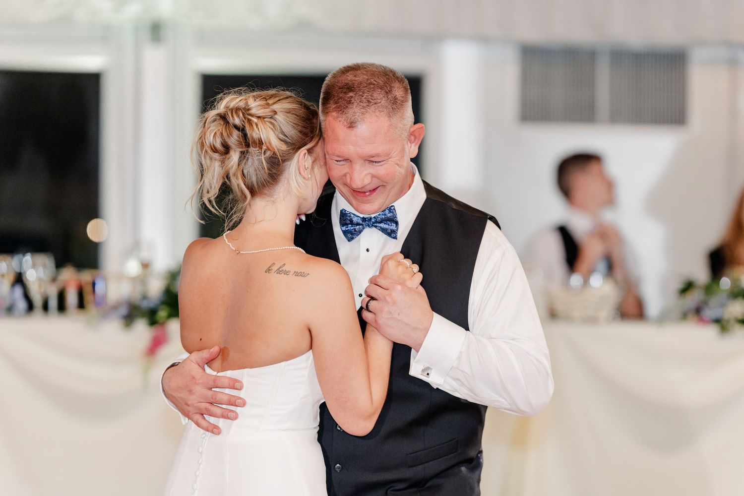 Bride and groom sharing an emotional first dance, groom in navy vest and blue bow tie.