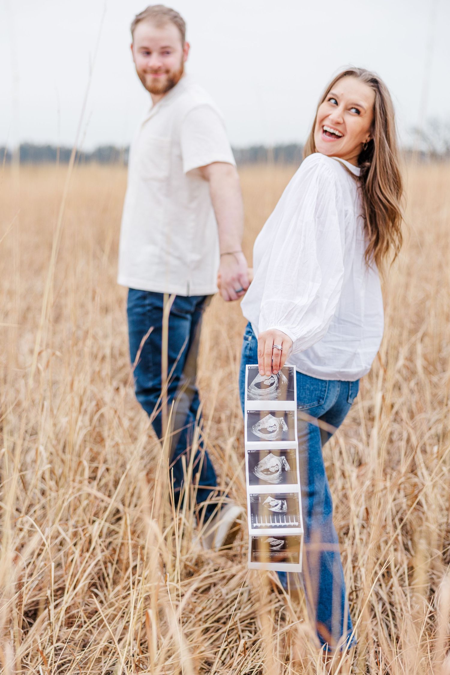Ultrasound photo strip held in tall grass during pregnancy announcement photos in Cary, Illinois