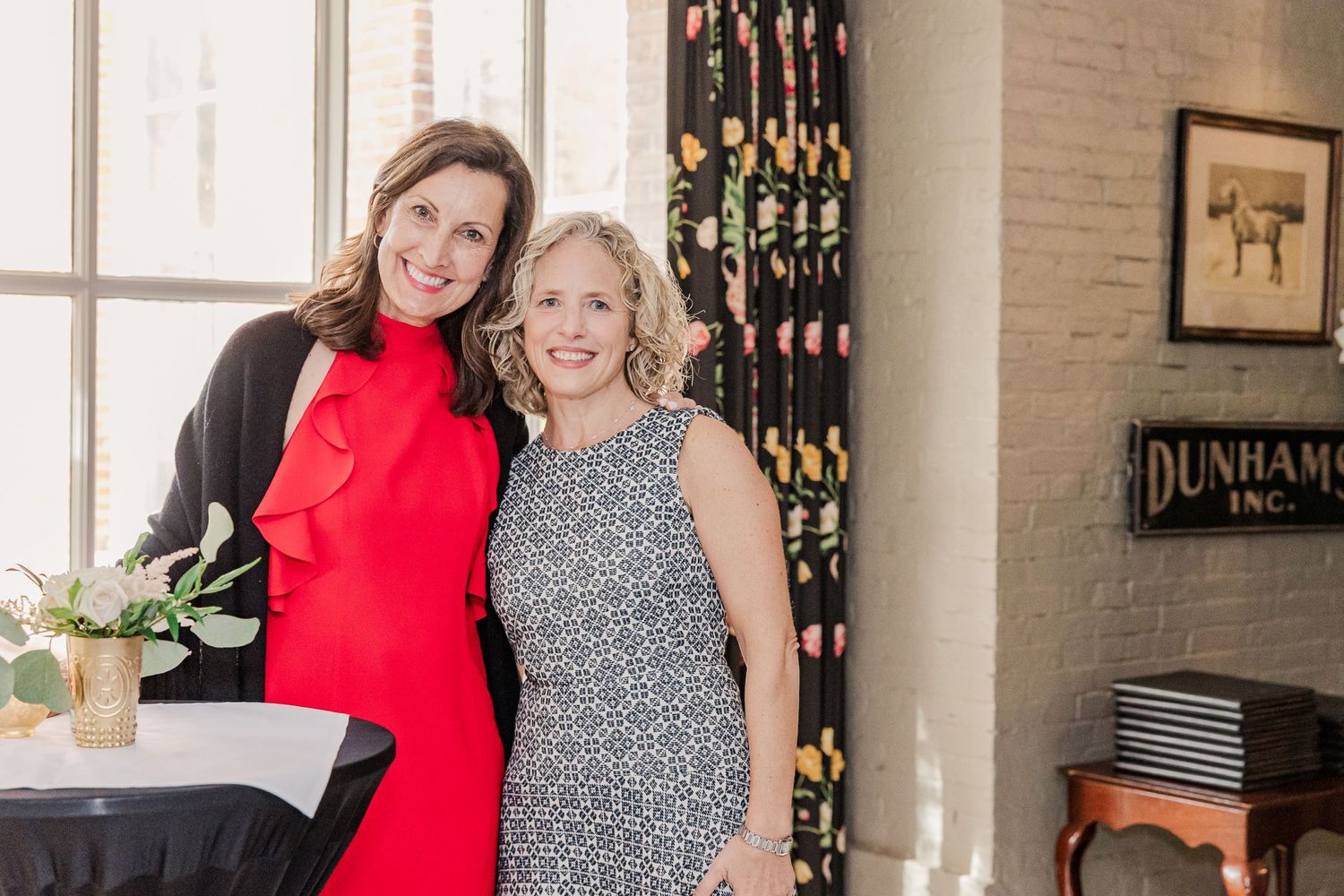 Two guests posing together at an elegant indoor event space with decorative curtains.