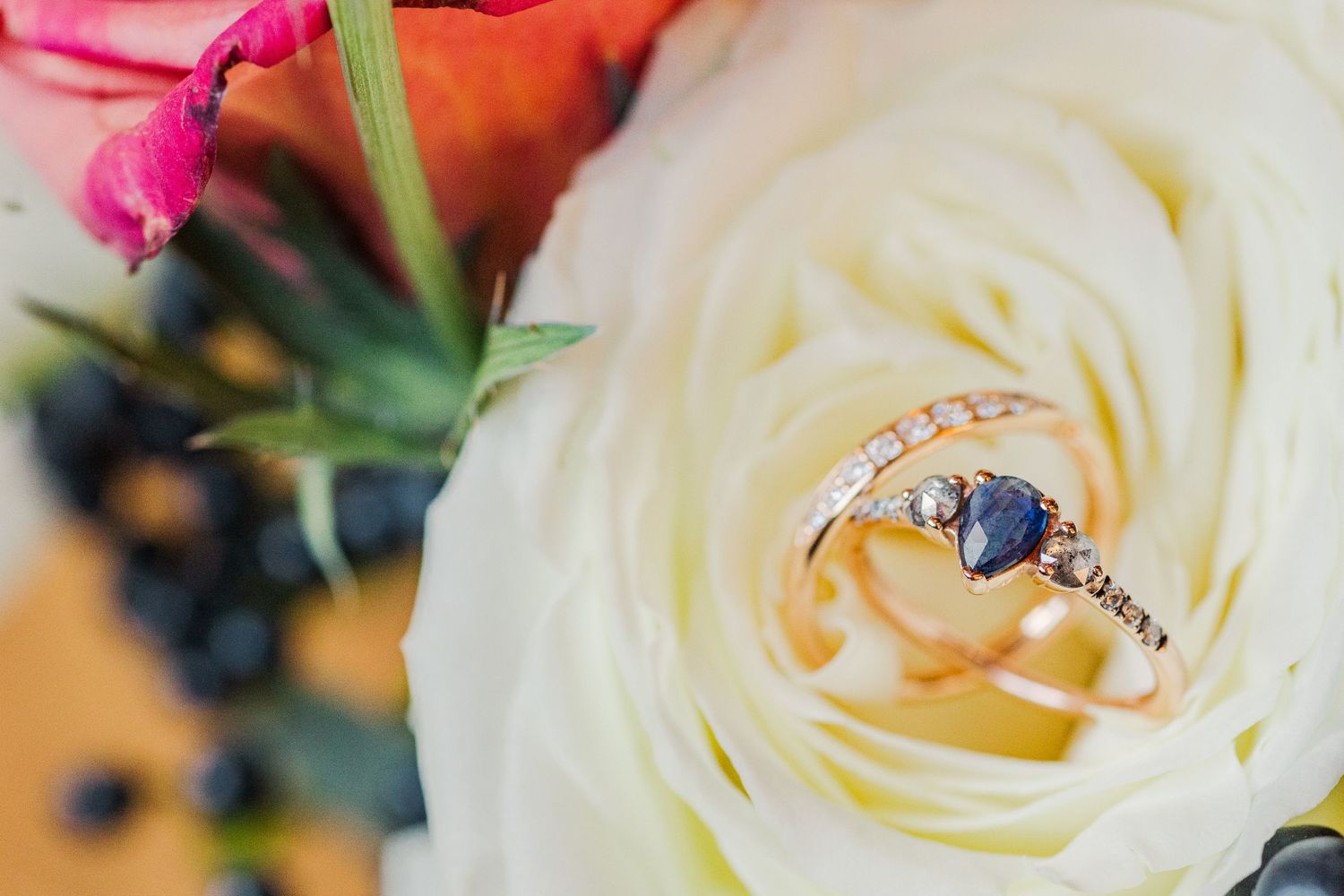 Diamond and sapphire engagement ring nestled in the center of a white rose bloom.