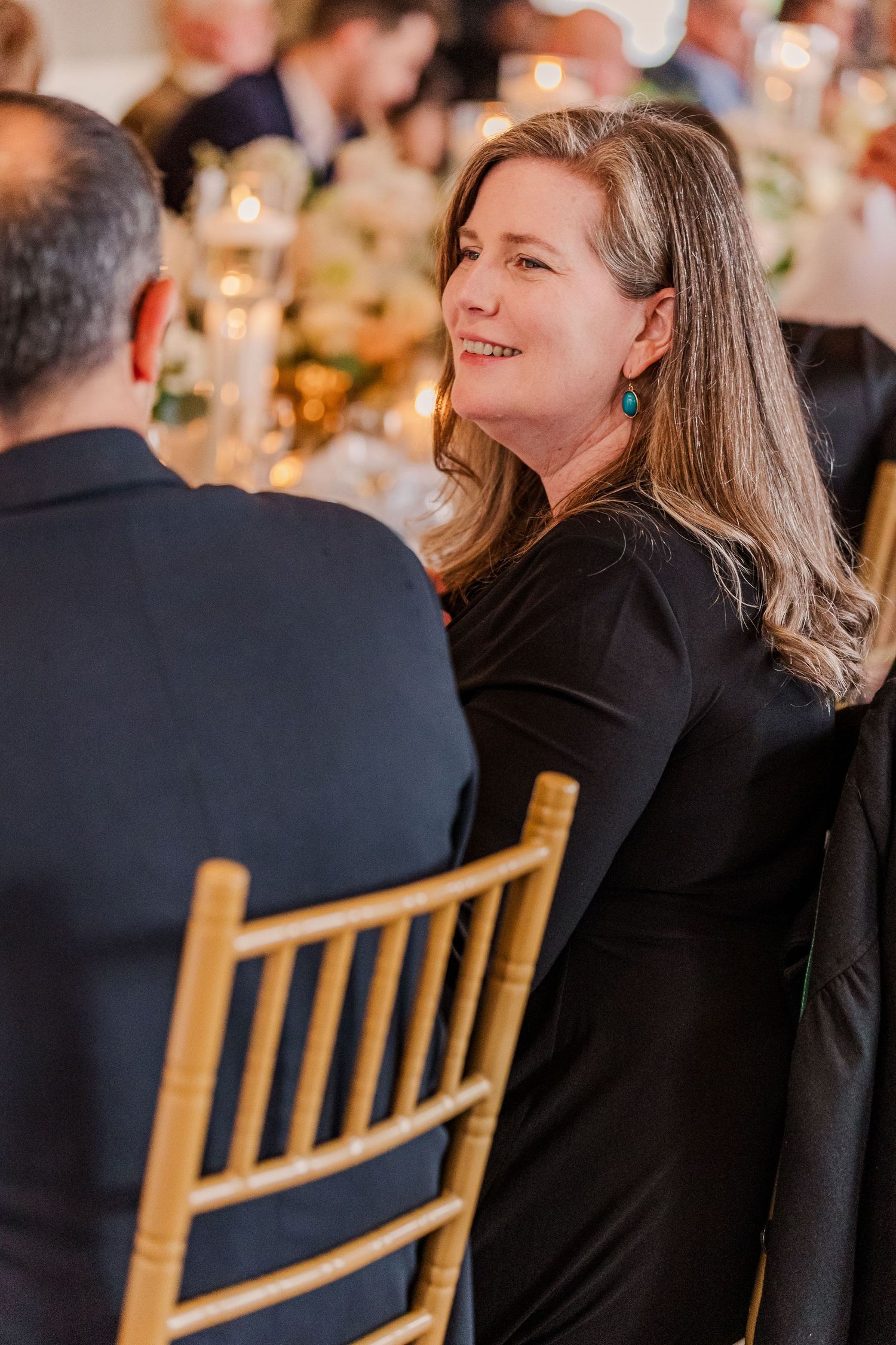 Guest in black dress smiling during formal dinner conversation.