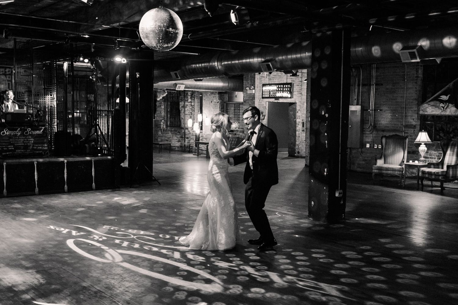 A romantic dance on a patterned light floor beneath a disco ball in a vintage industrial space.