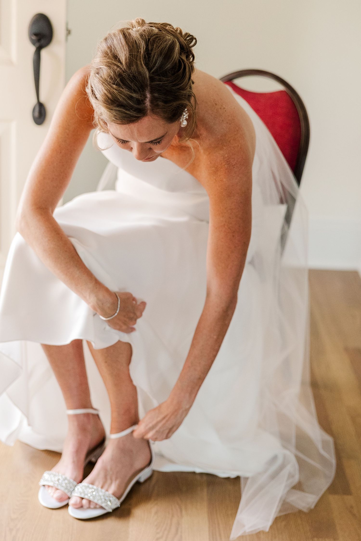 Person in white wedding dress putting on sparkly bridal shoes.