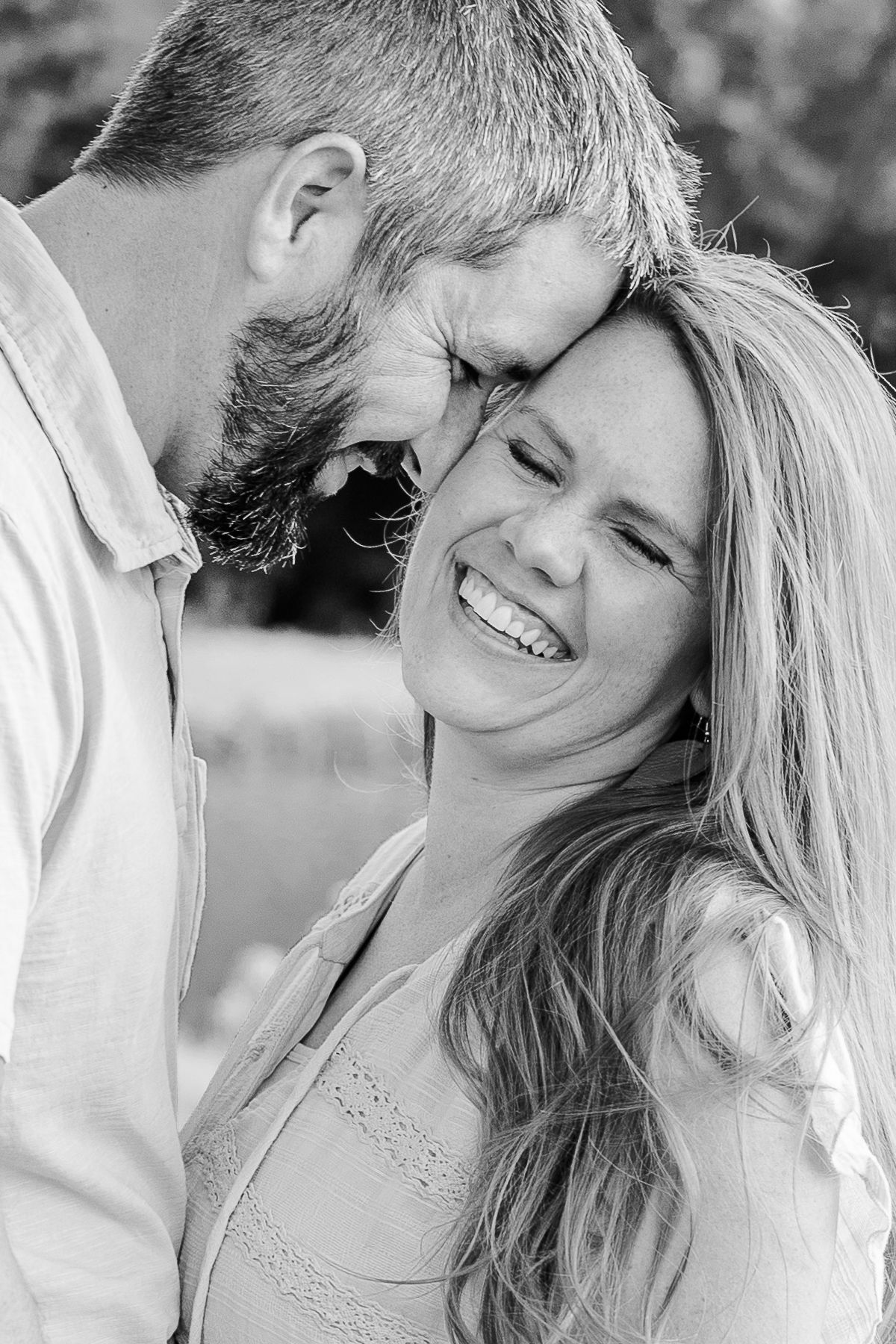 A black and white intimate portrait of a couple sharing a tender moment outdoors.