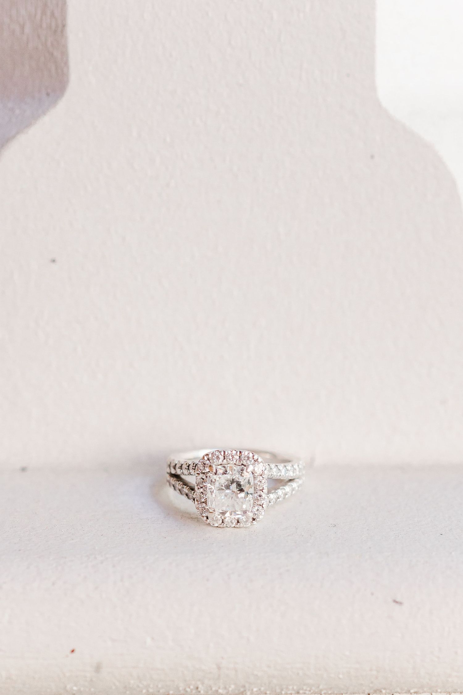 Diamond engagement ring with square halo setting displayed on white surface.