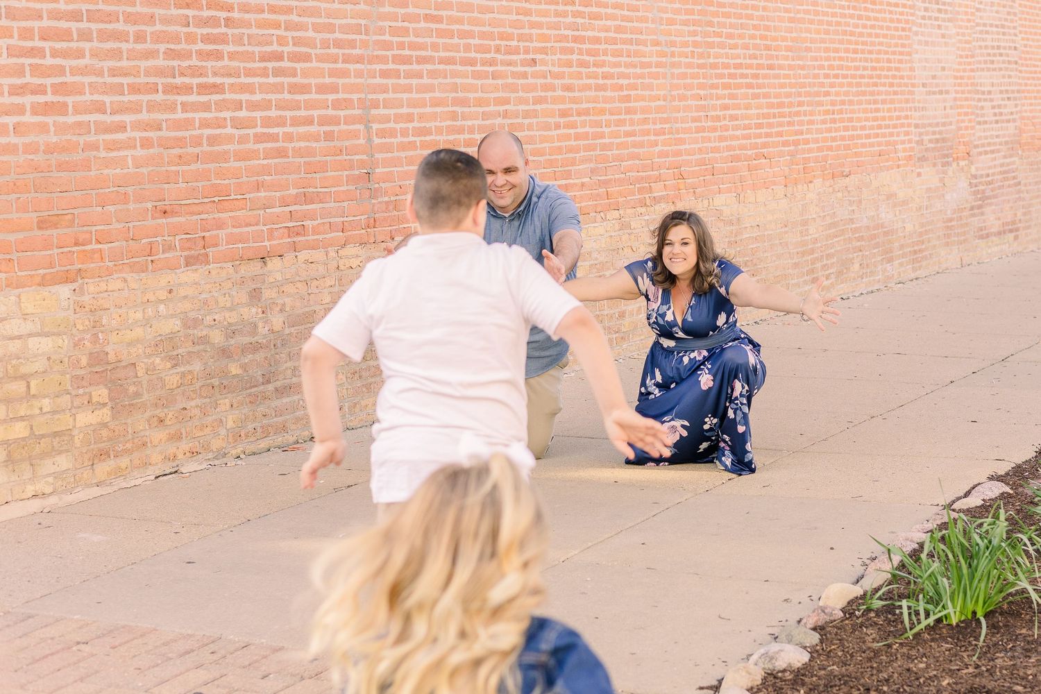 Family members pose and interact playfully against brick wall backdrop.