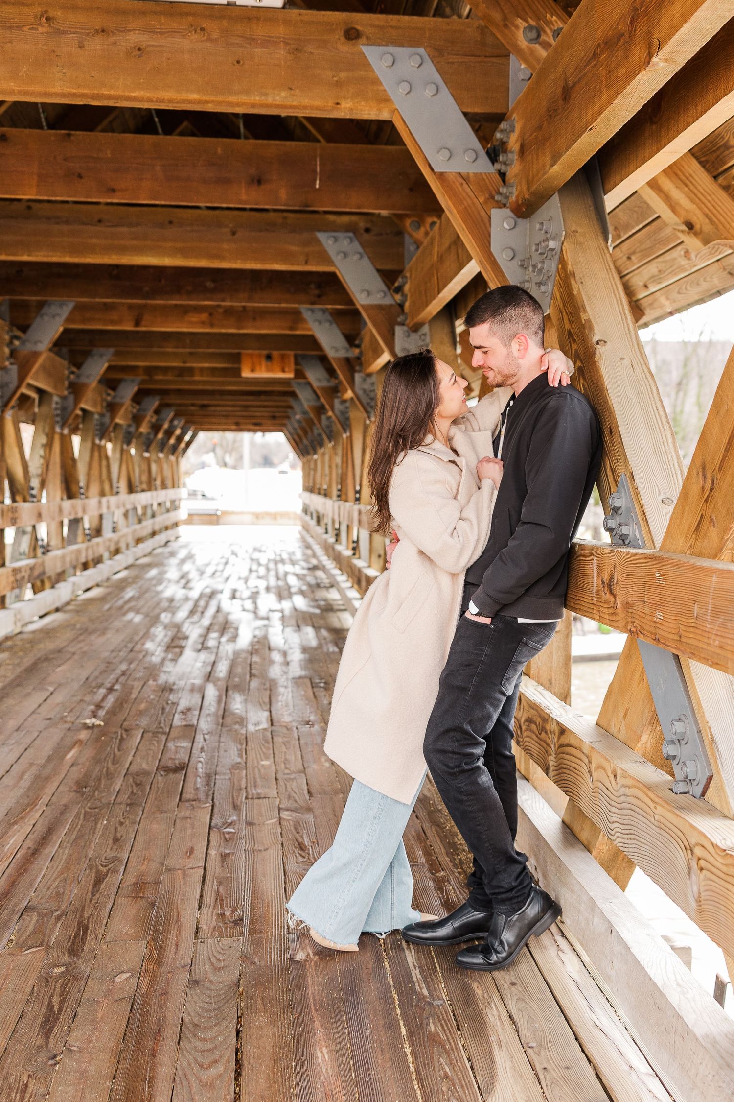 A romantic couple embracing against the wooden walls of a covered bridge.