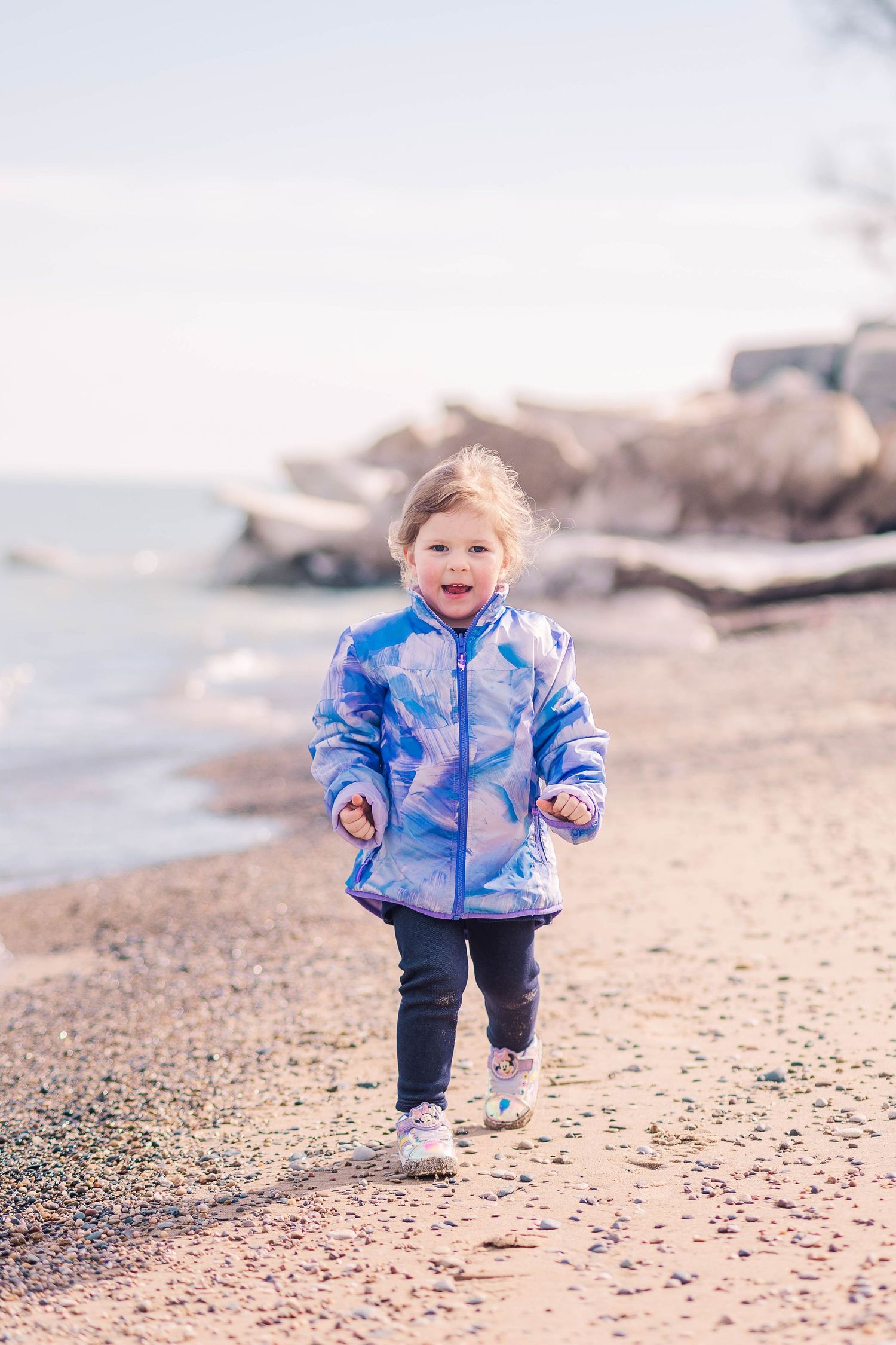Someone runs joyfully along a rocky beach wearing a blue patterned winter jacket.