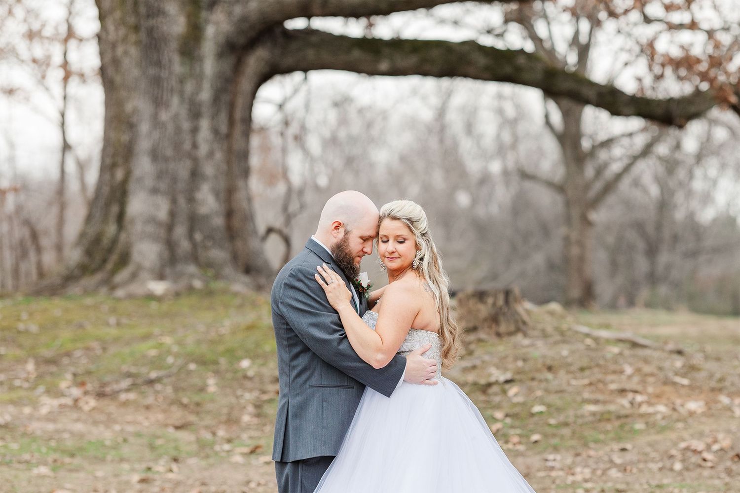 Intimate wedding moment photographed in a rustic outdoor setting with bare winter trees.