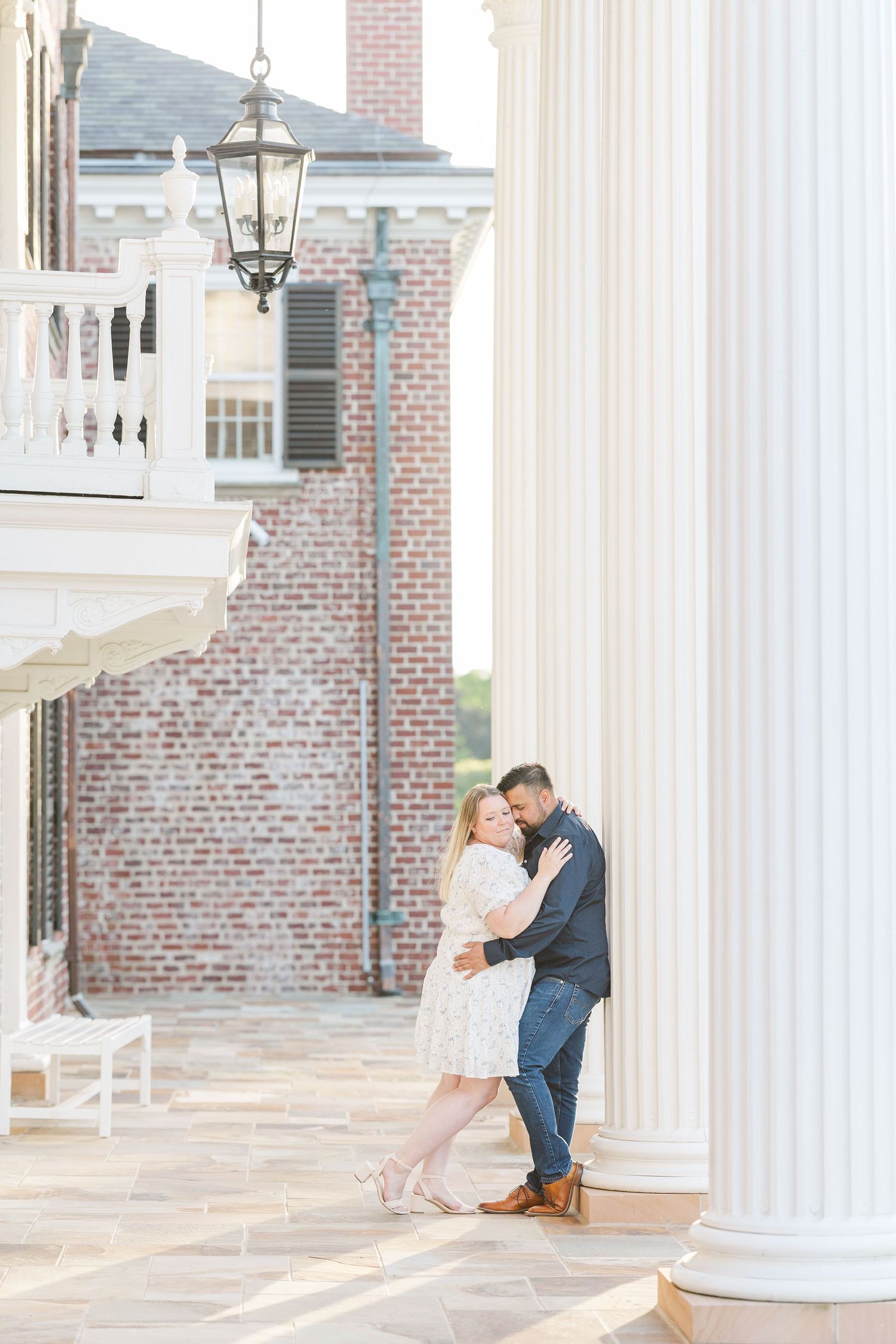 Romantic portrait under an antique lamp post near white columns and brick walls.