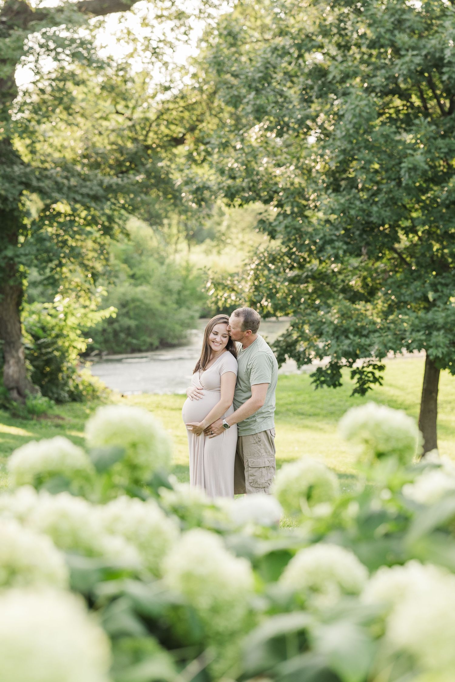 Romantic moment captured in a garden setting with lush greenery and white hydrangea flowers in soft sunlight.