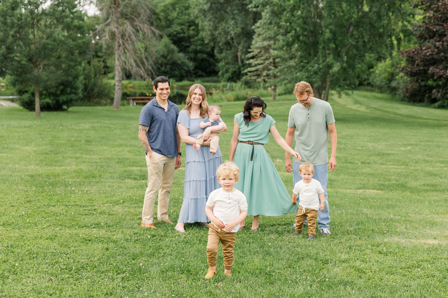 Extended family of six posing on green lawn with toddler standing in foreground.