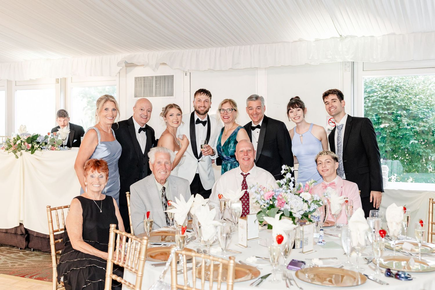 Wedding party and family pose together for group photo at elegant white tent reception dinner.