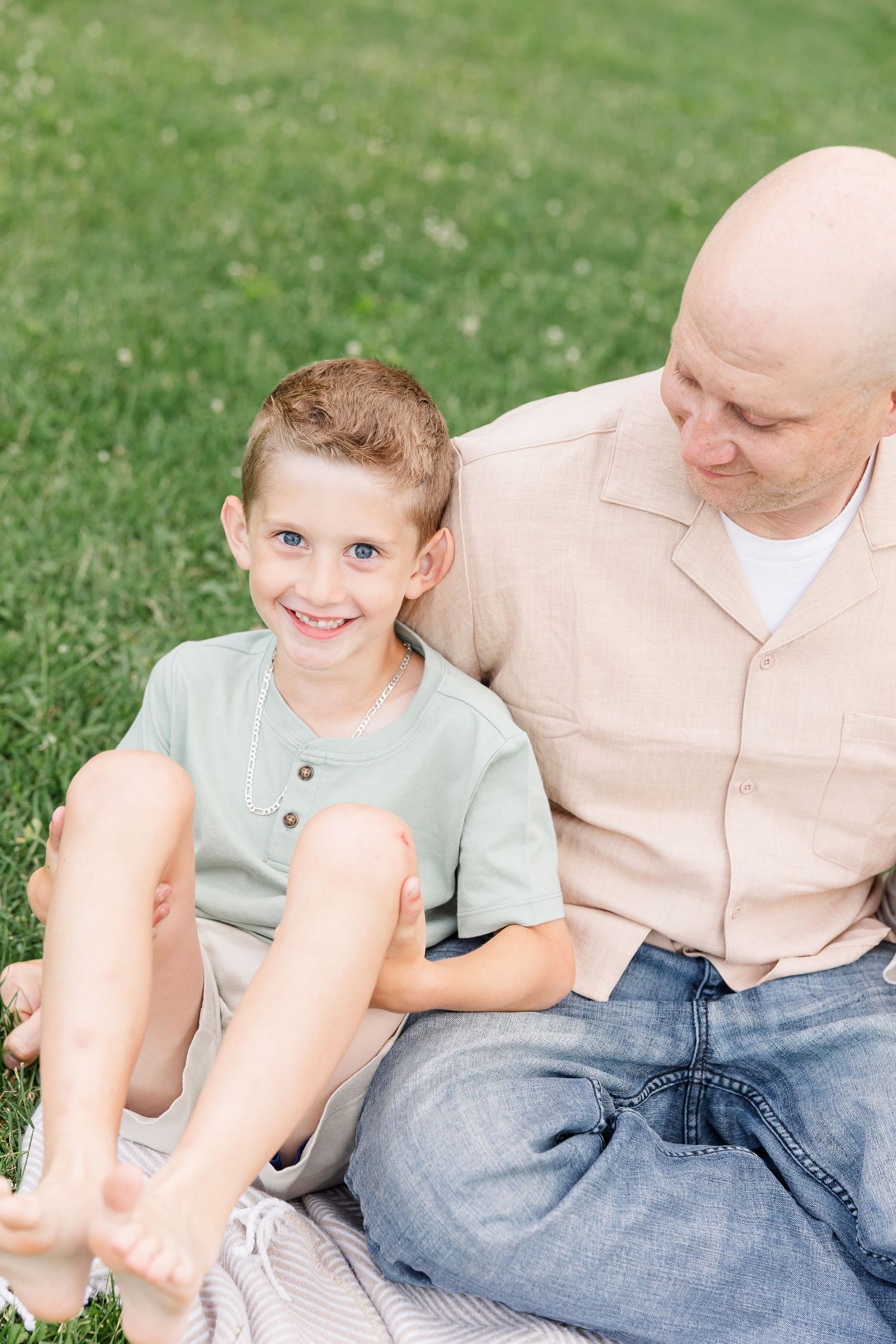 Young boy sitting beside his dad during a summer family portrait session in Crystal Lake, Illinois.