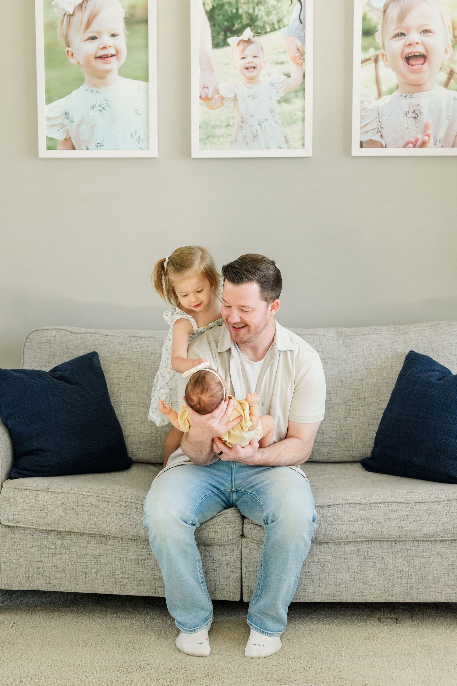 Dad holding baby girl while big sister looks on during a cozy newborn session at home
