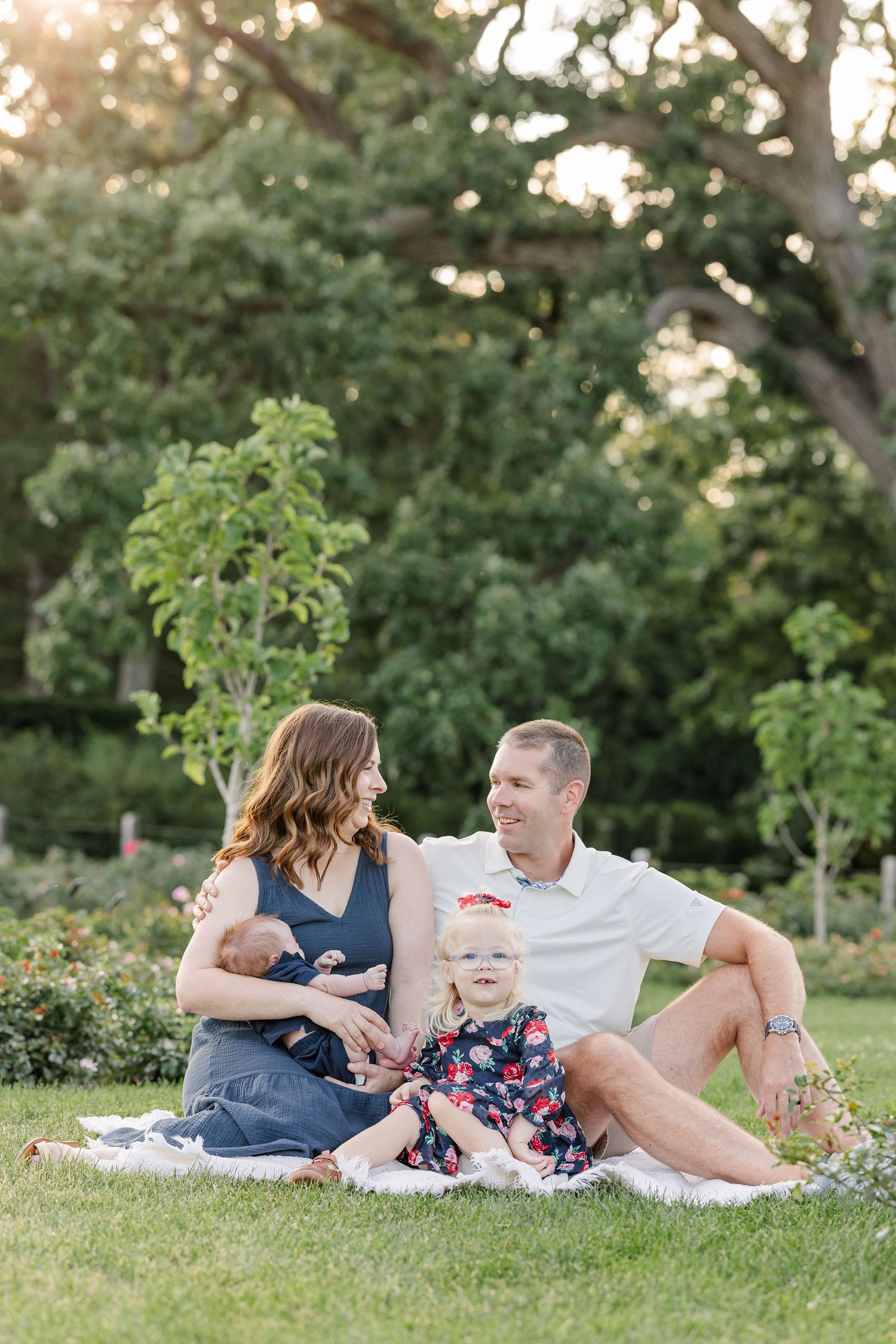 Hilary and Andrew smiling at each other while sitting with Caroline and newborn Lincoln at Cantigny Park.